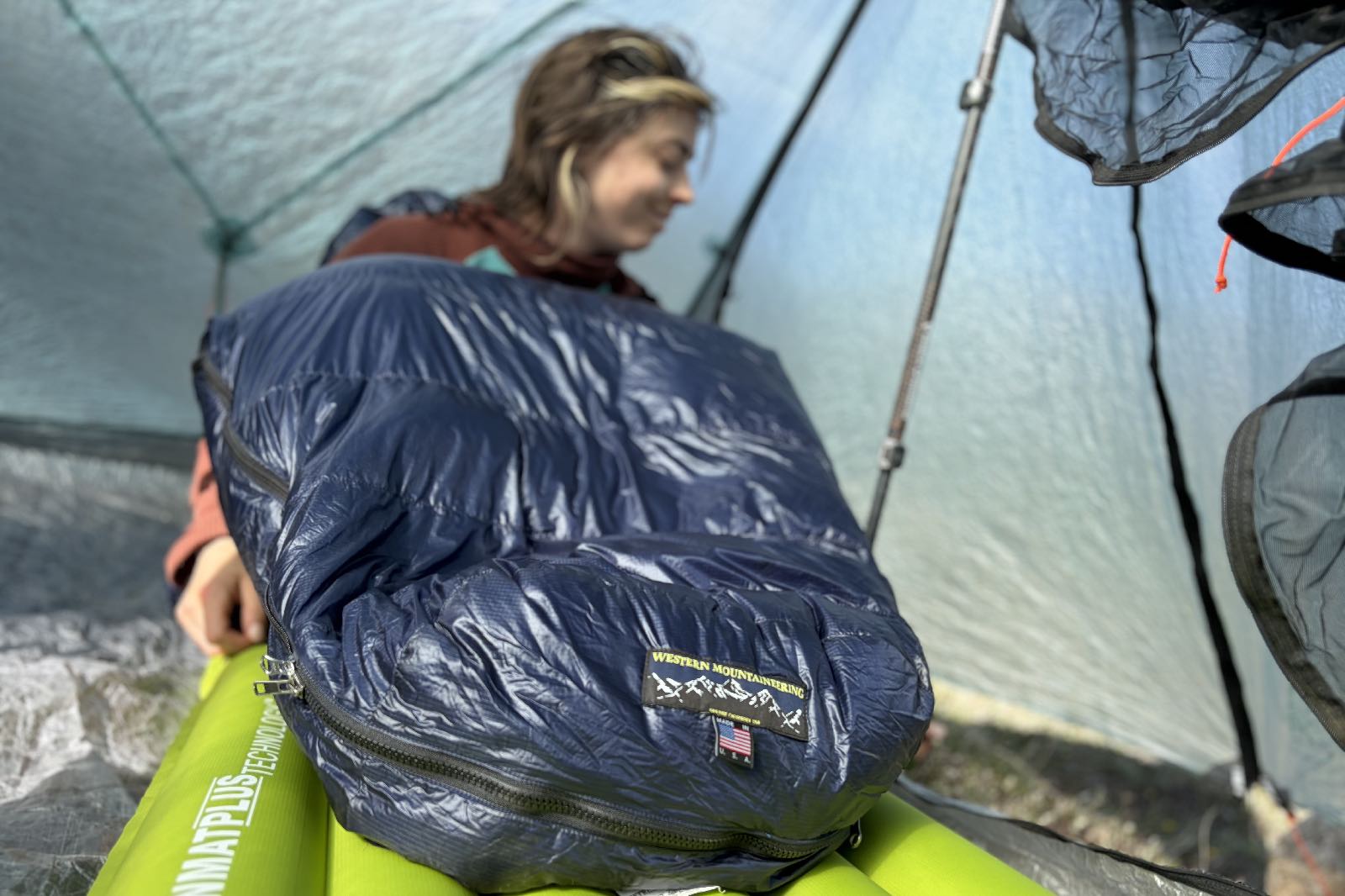 a hiker sits in a sleeping bag with her feet to the camera