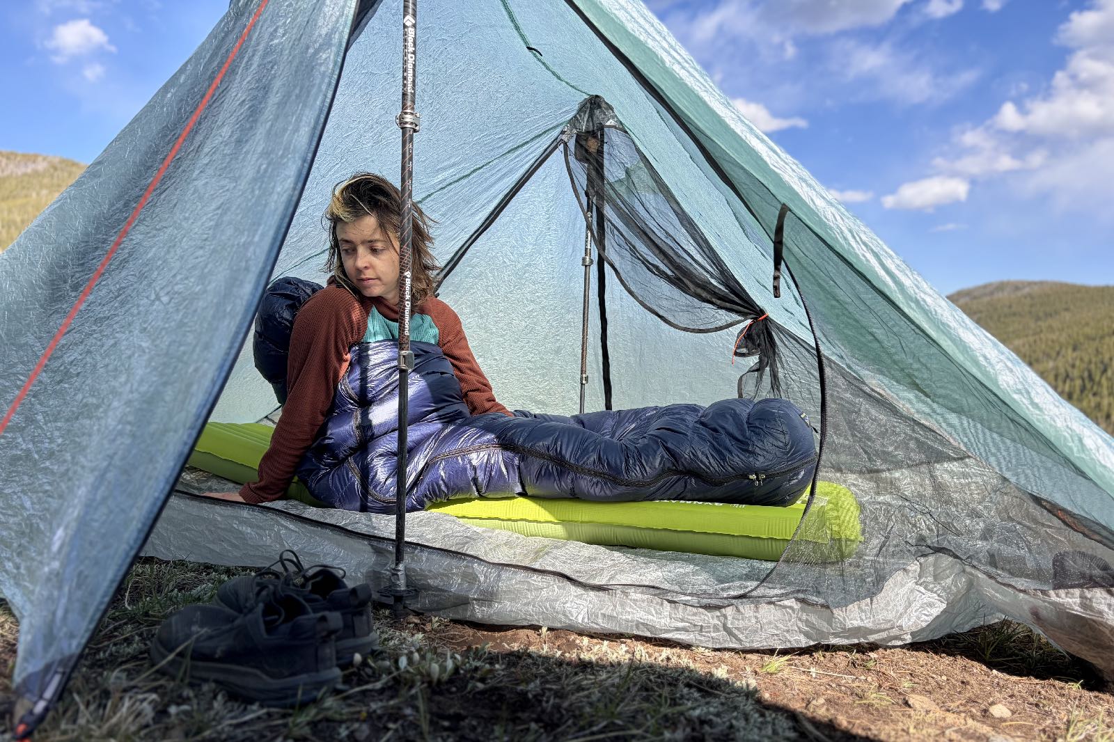 a hiker sits up in a tent in a sleeping bag