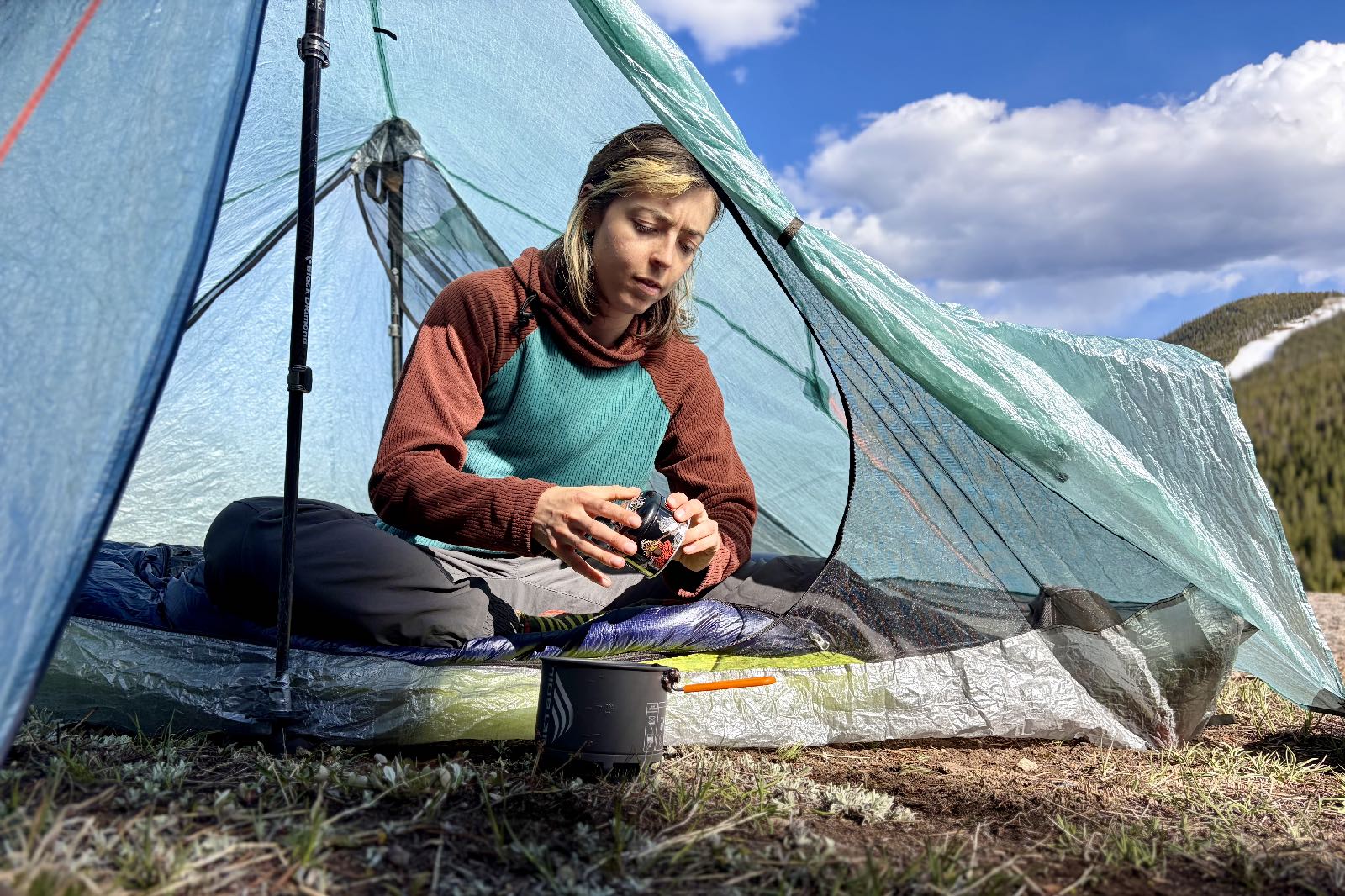 A hiker sits in a tent preparing to cook on a backpacking stove.