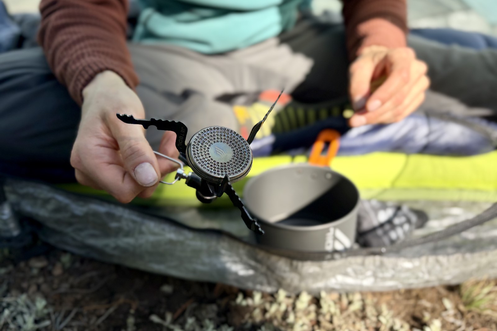 A hiker shows off a small backpacking stove with notches in its pot support.