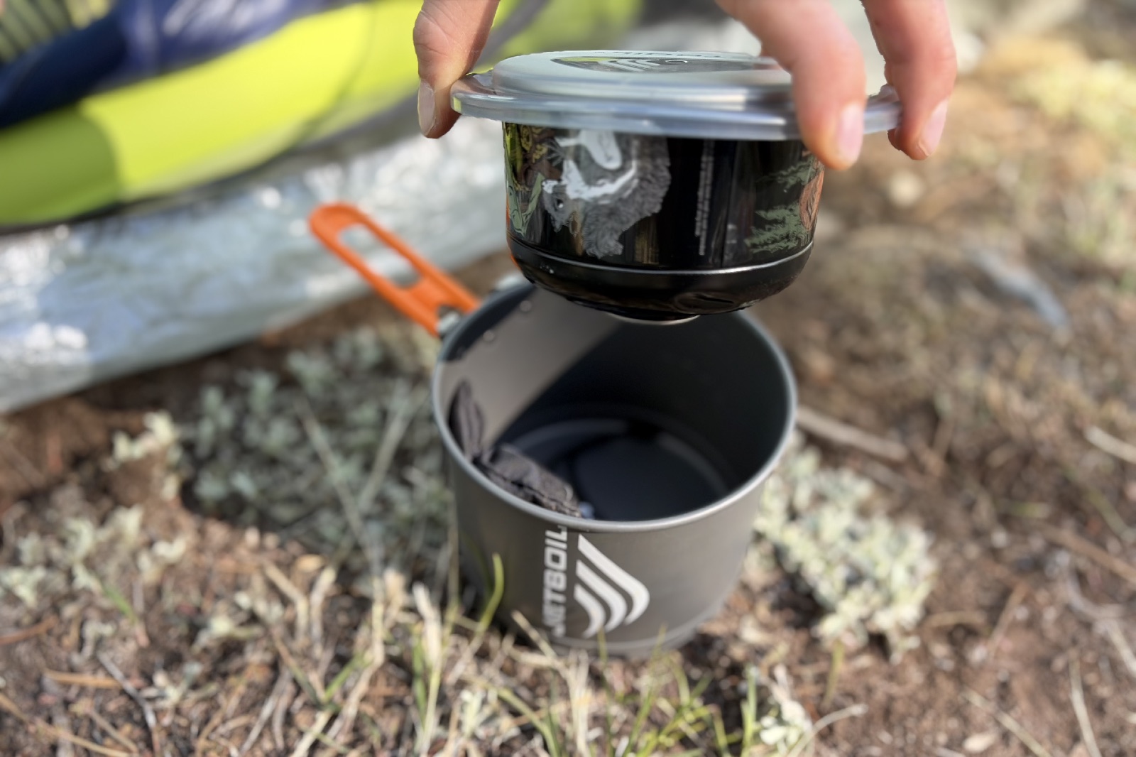 A hiker pulls the lid with a fuel canister attached off of a cook set.