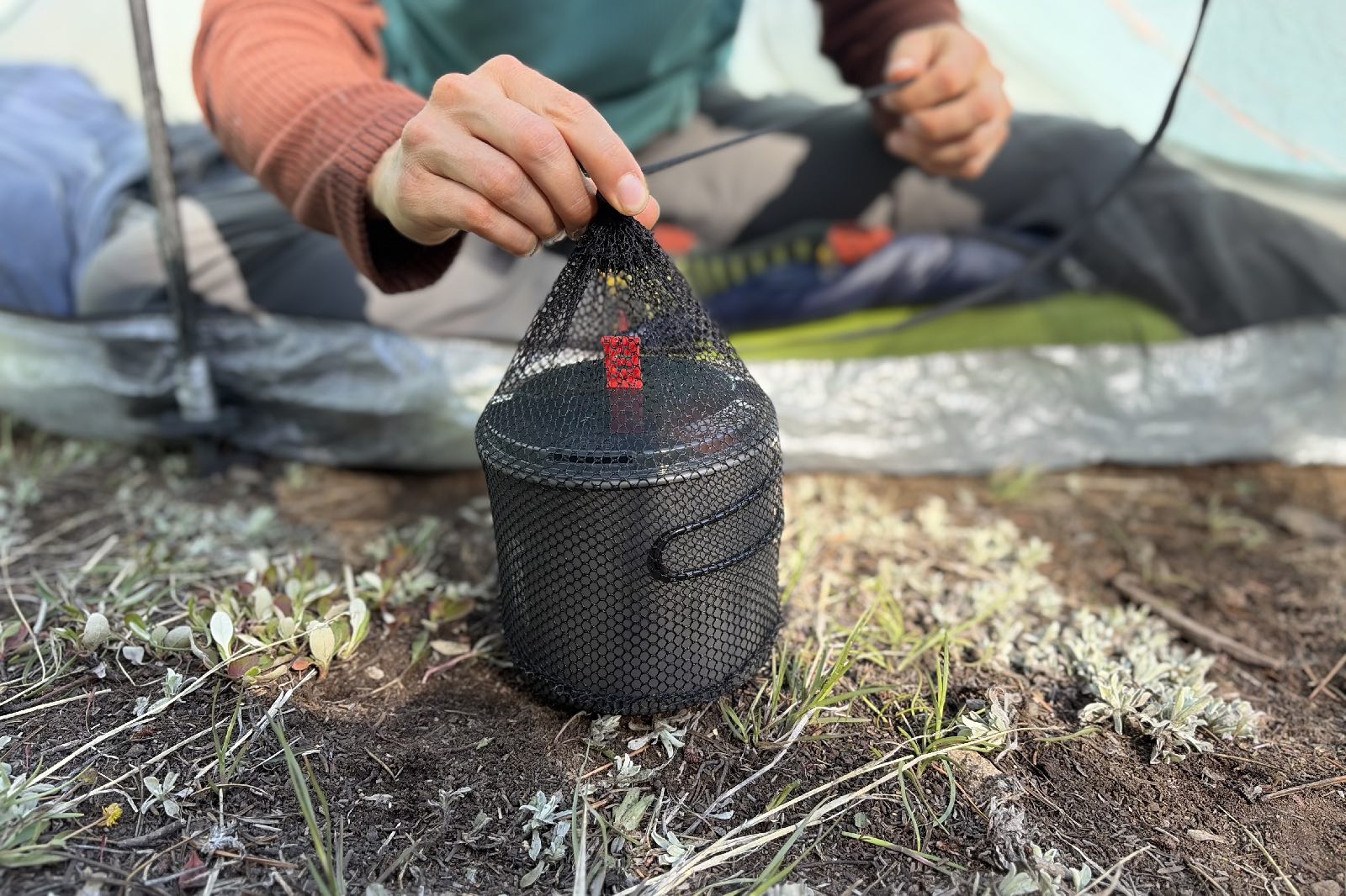 a hiker sits in a tent while cinching the stuff sack closed on her cook kit