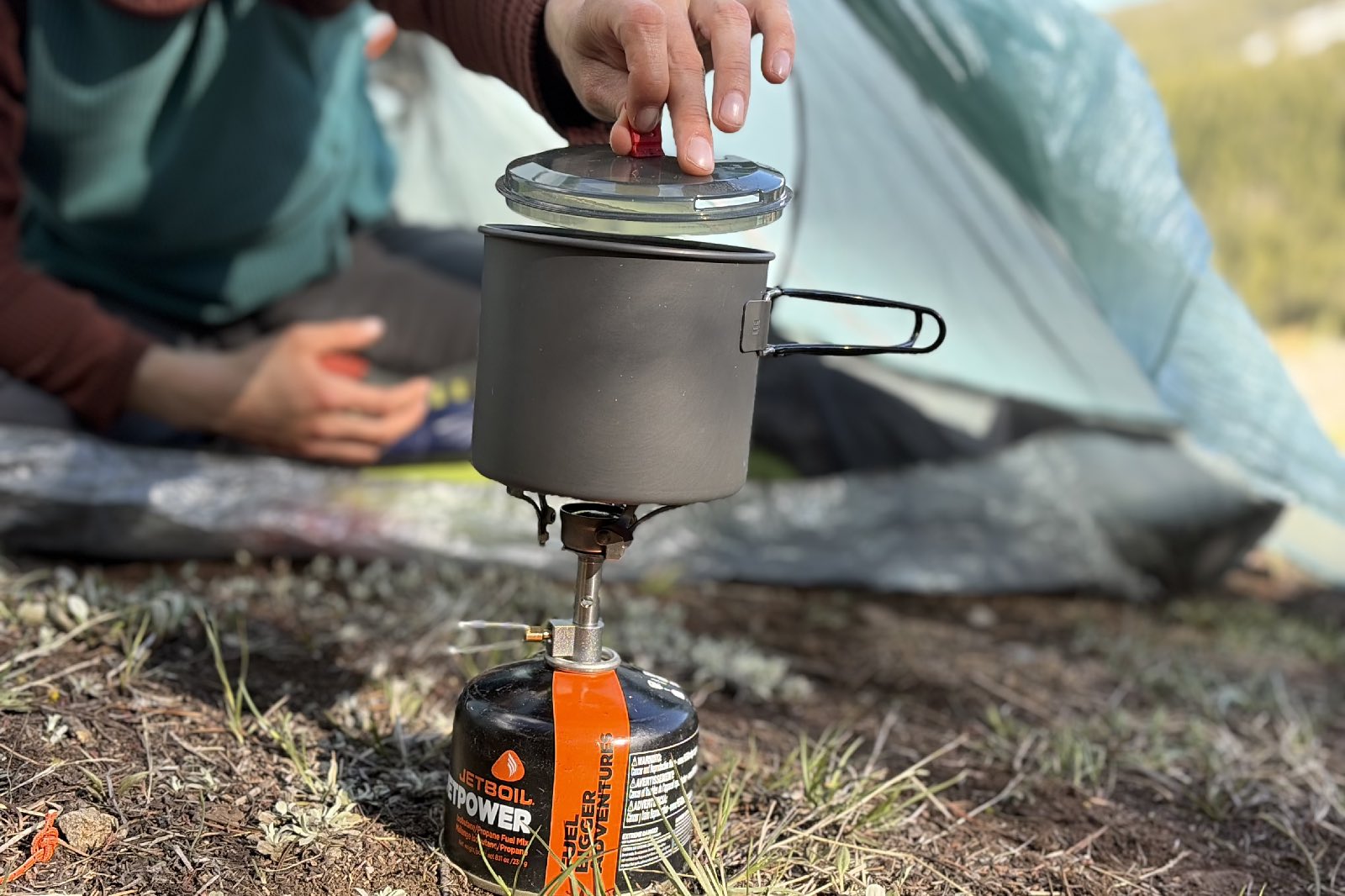 a hiker lays in a tent a lifts the lidd off her cook pot