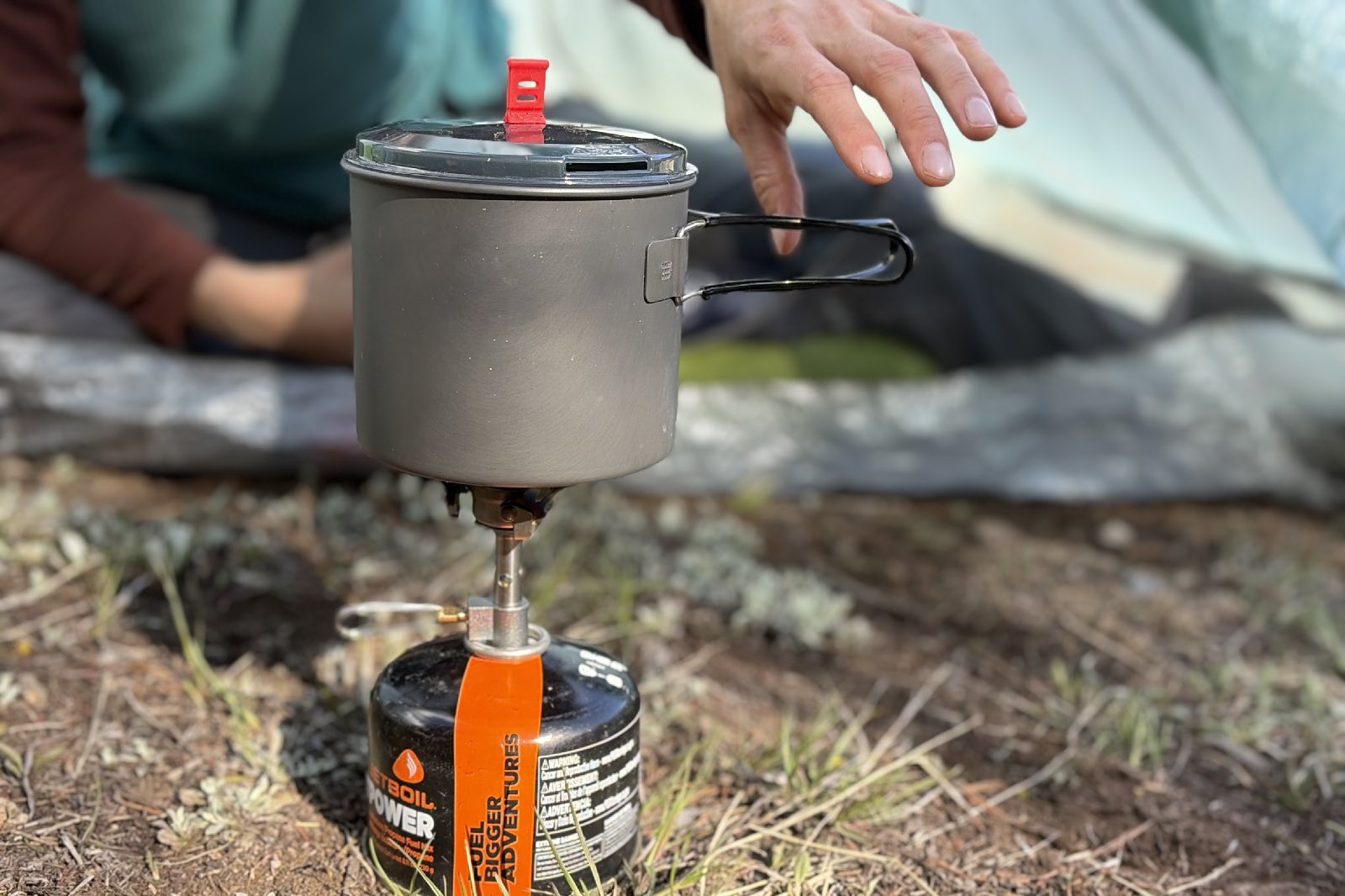 a hand reaches for a backpacking pot on a stove