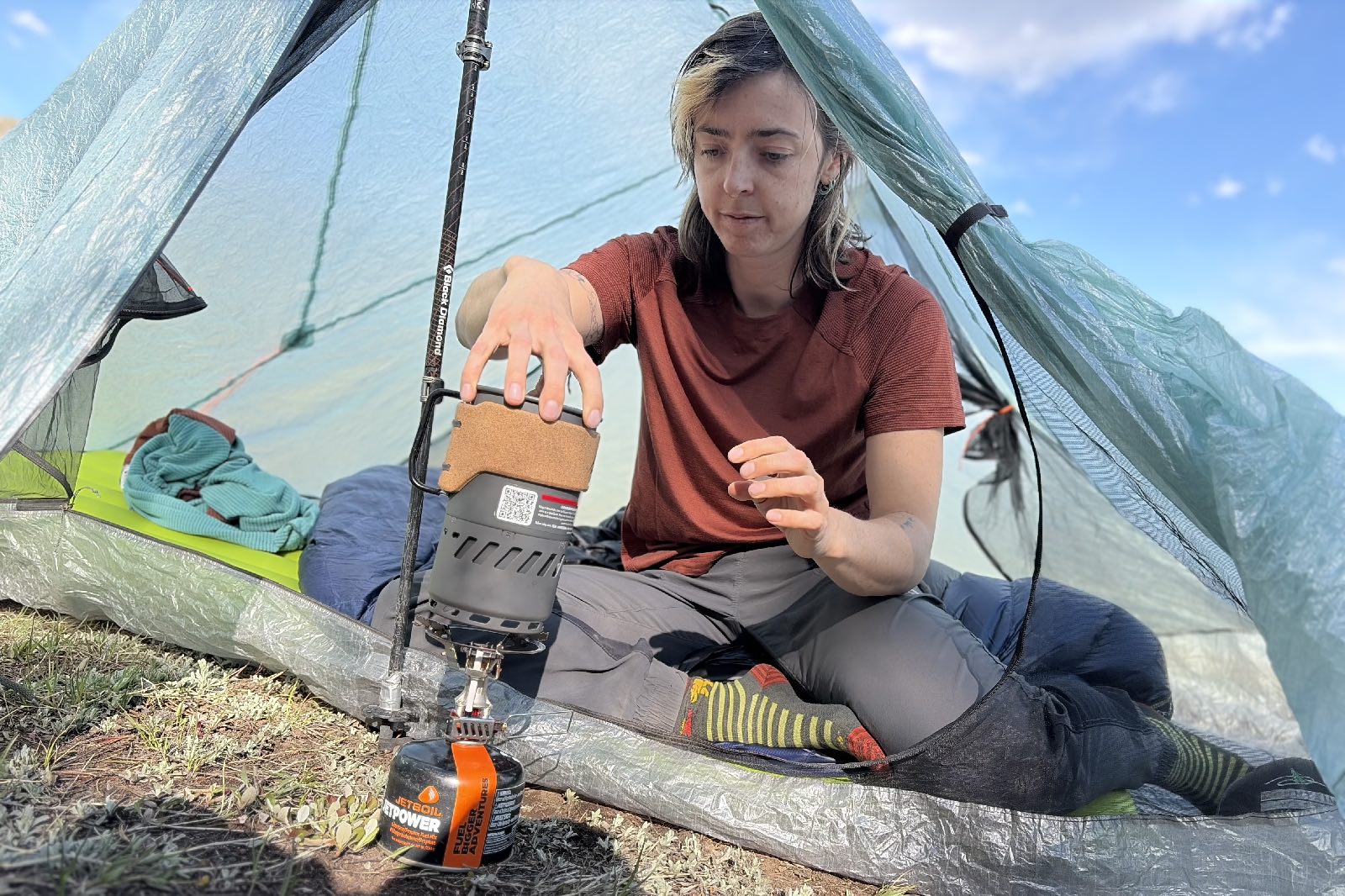 A hiker sits in a tent cooking with a backpacking stove.
