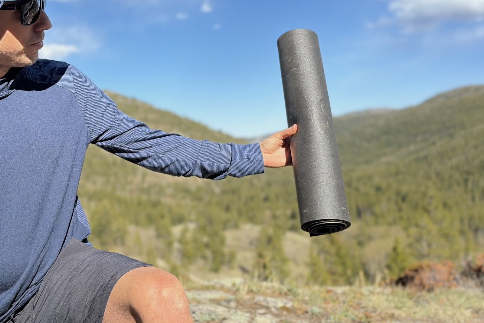 A hiker holds a grey rolled up sleeping pad