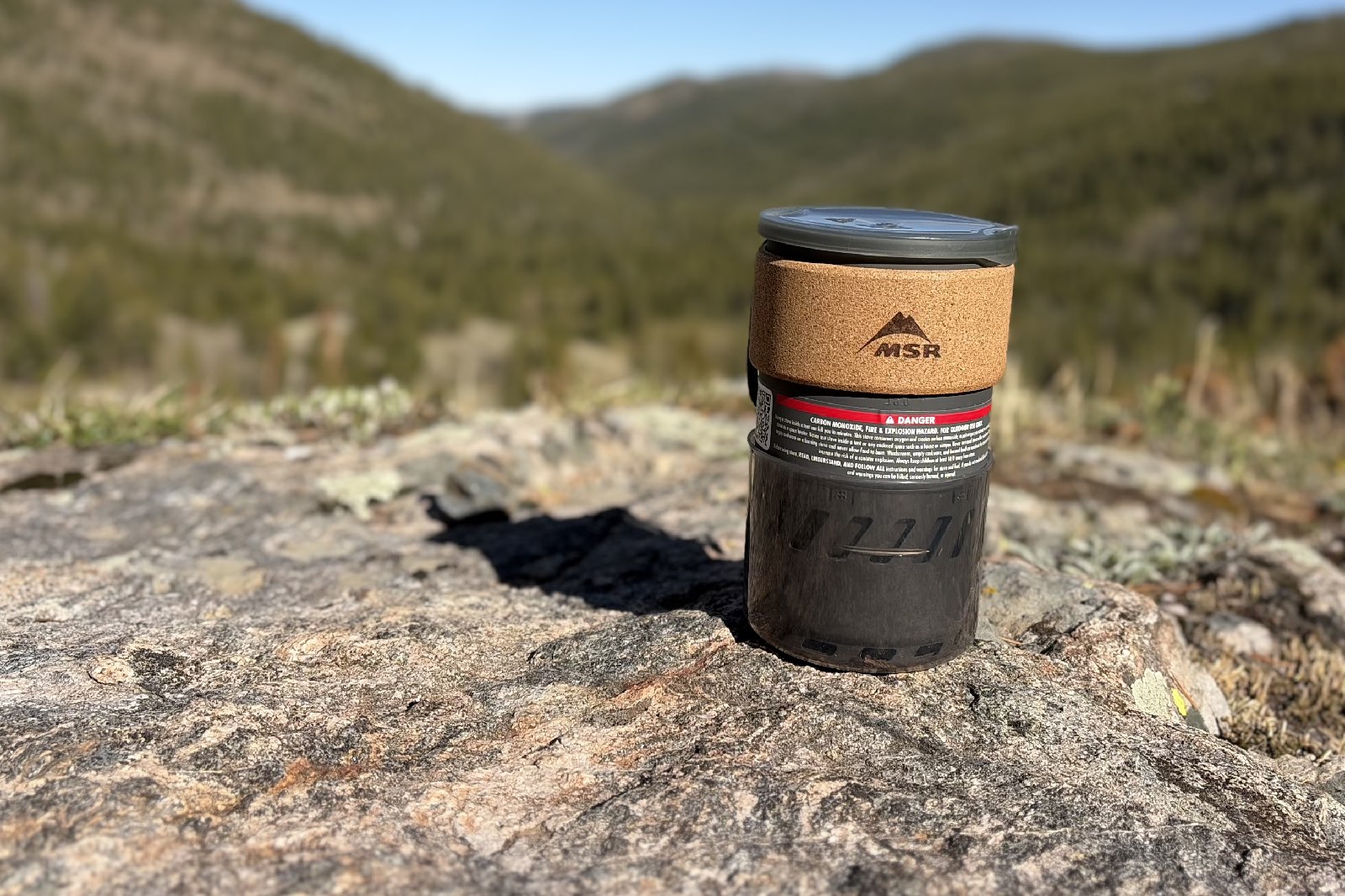 A backpacking cook kit sitting on a rock overlooking at a beautiful mountain view.
