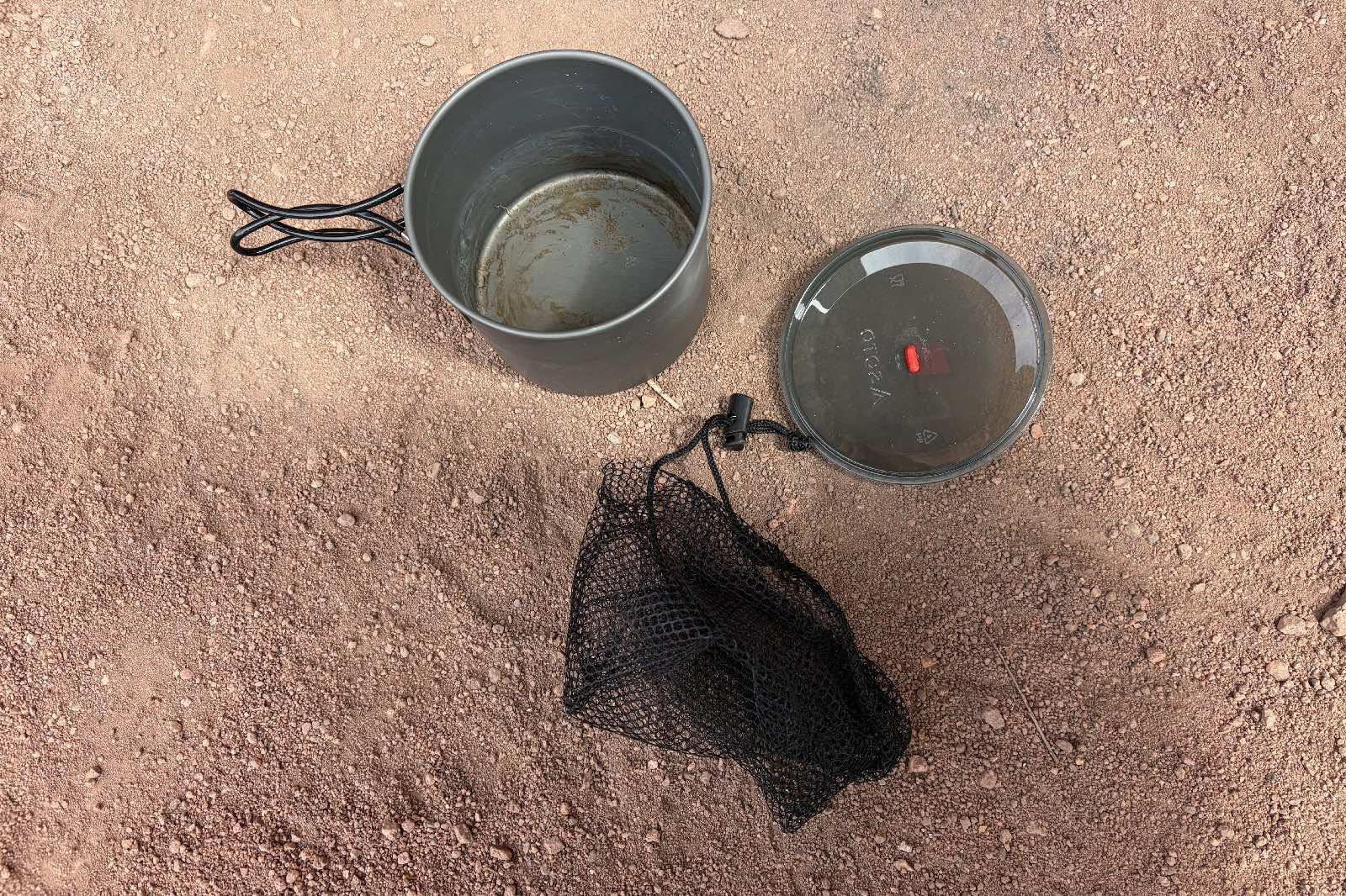 components of a backpacking pot sit in the sand
