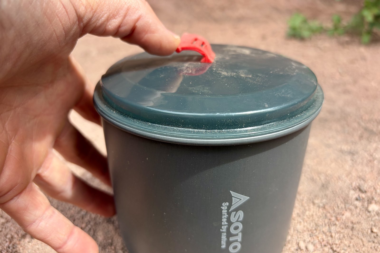 a close up of a hand bending the lid handle of a backpacking pot