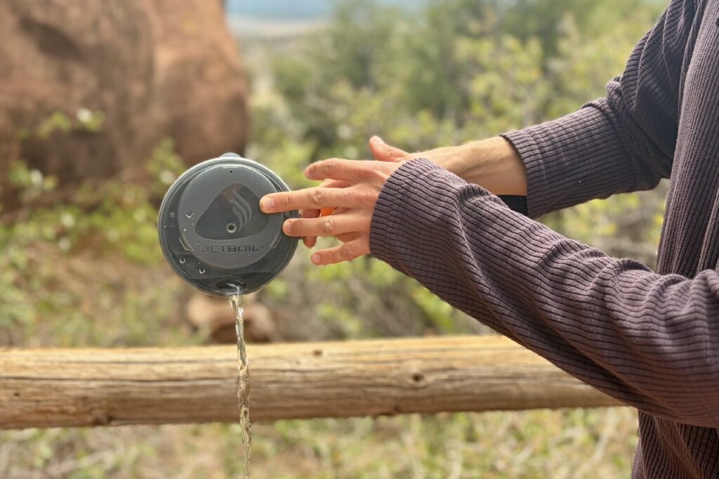 A person pours water through the pour spout lid of a Jetboil pot.