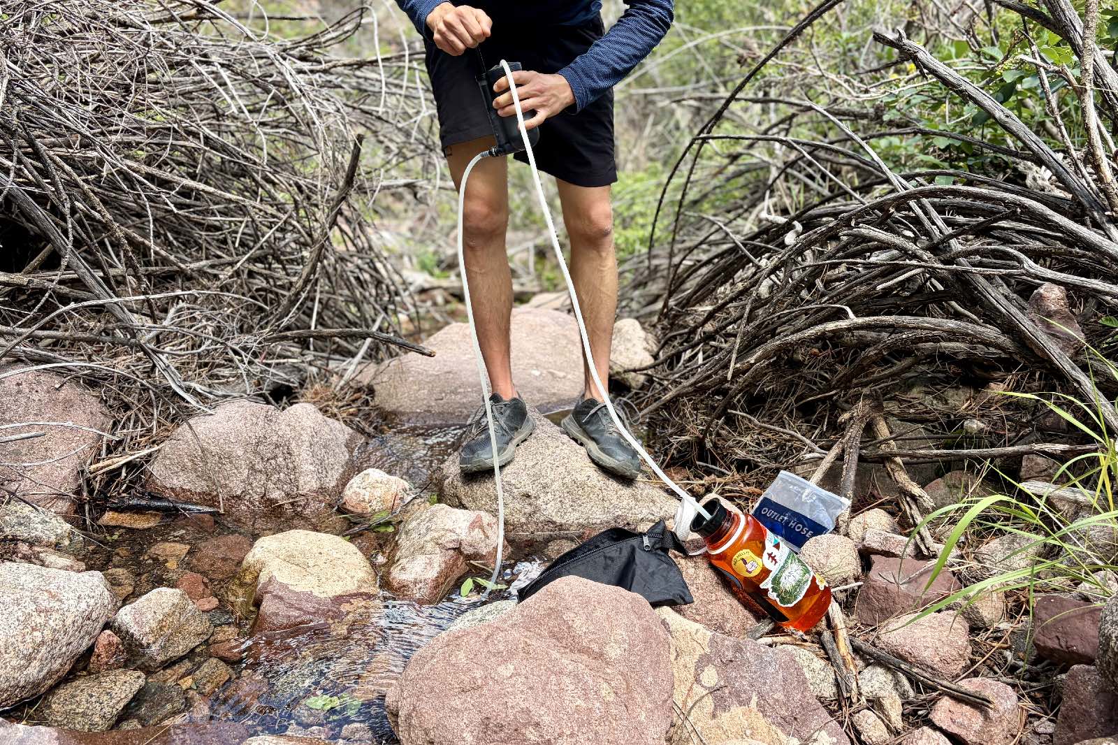 A hiker pumps water from a stream into a water bottle.