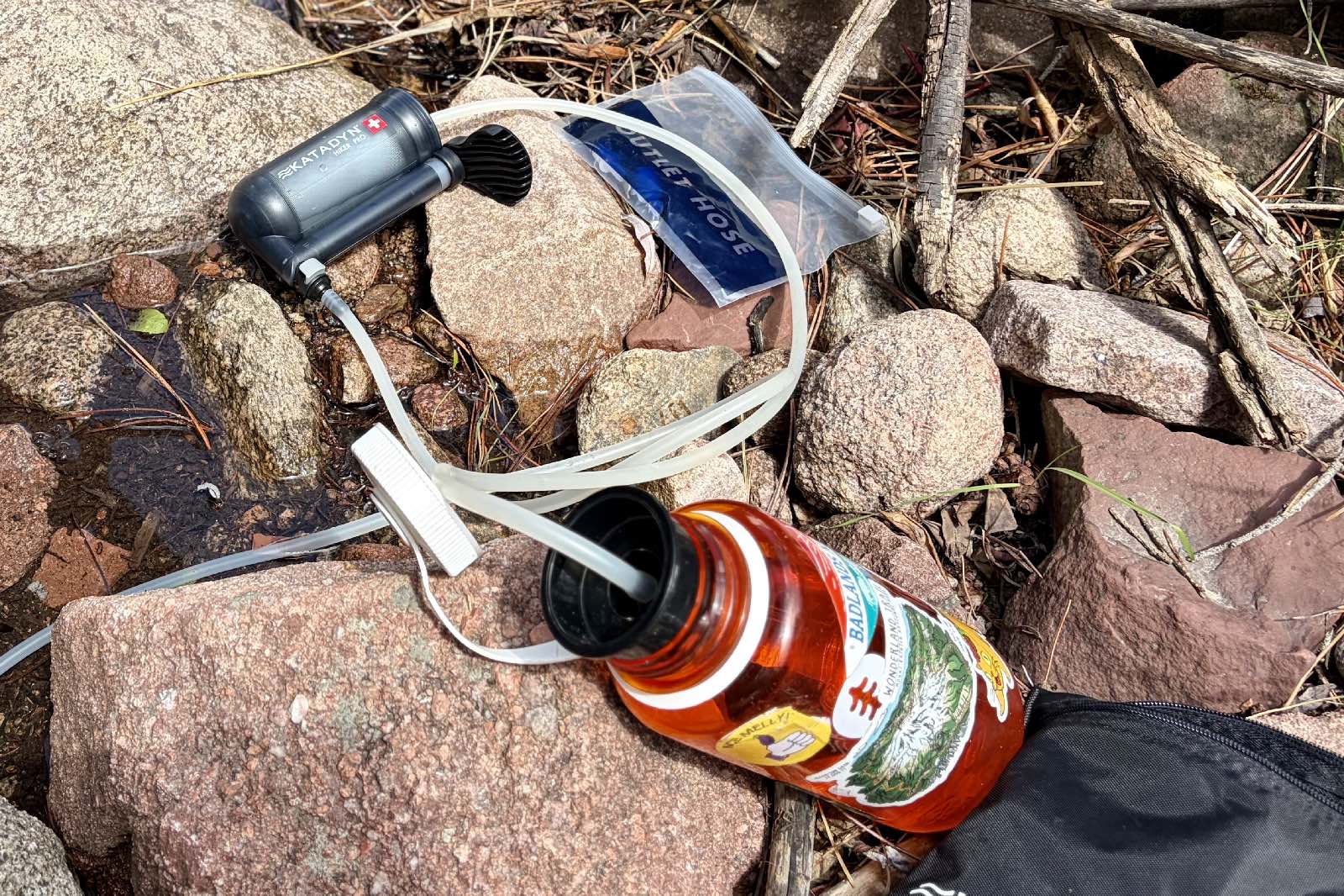 A water filter and all of its components sitting on some rocks.
