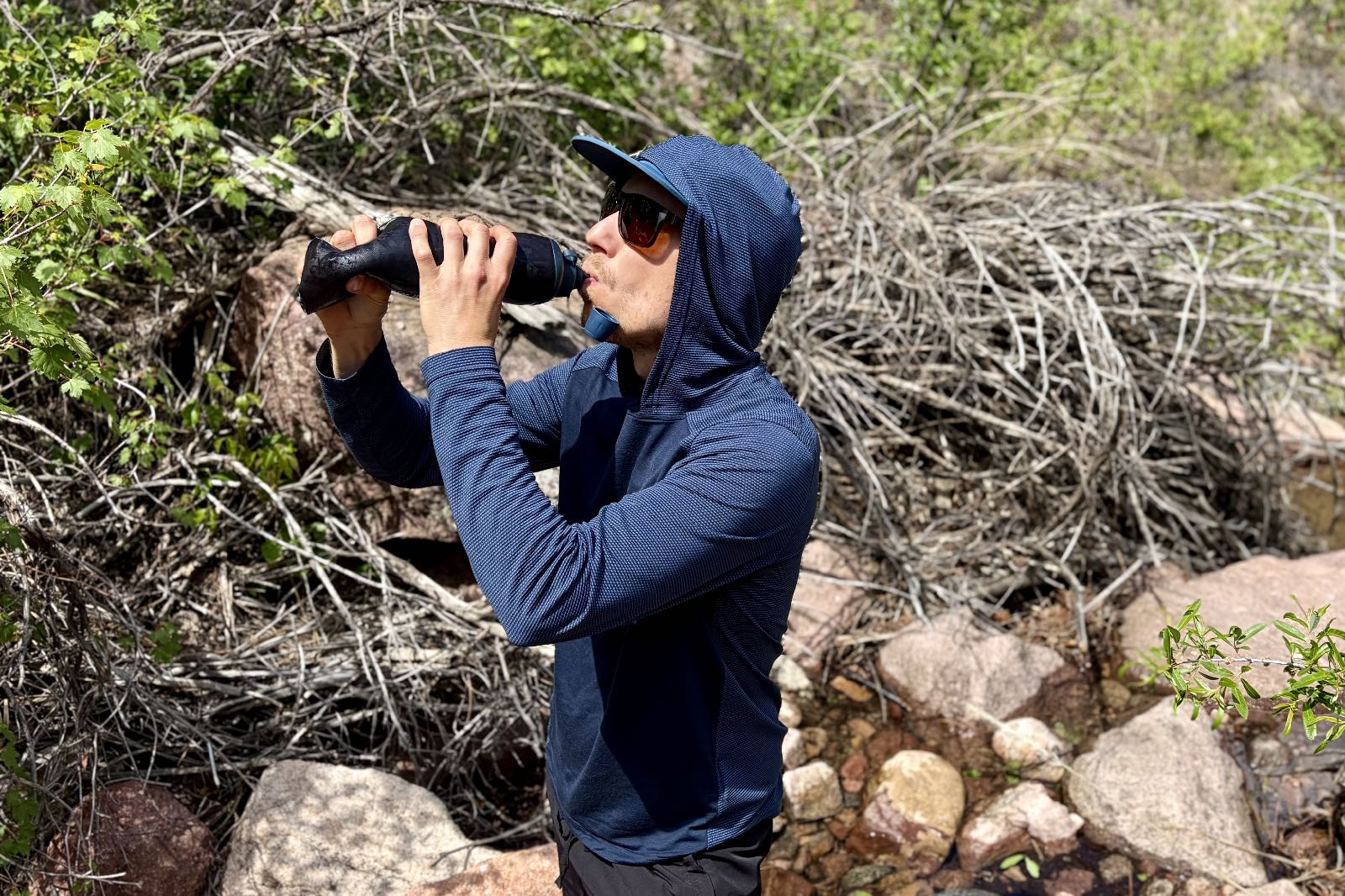 A hiker drinks from a soft flask water bottle.