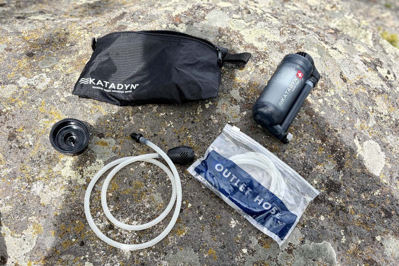 A water filter and all of its components sitting on a rock.
