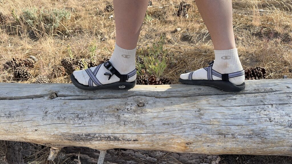 A woman walks along a log wearing black sandals.