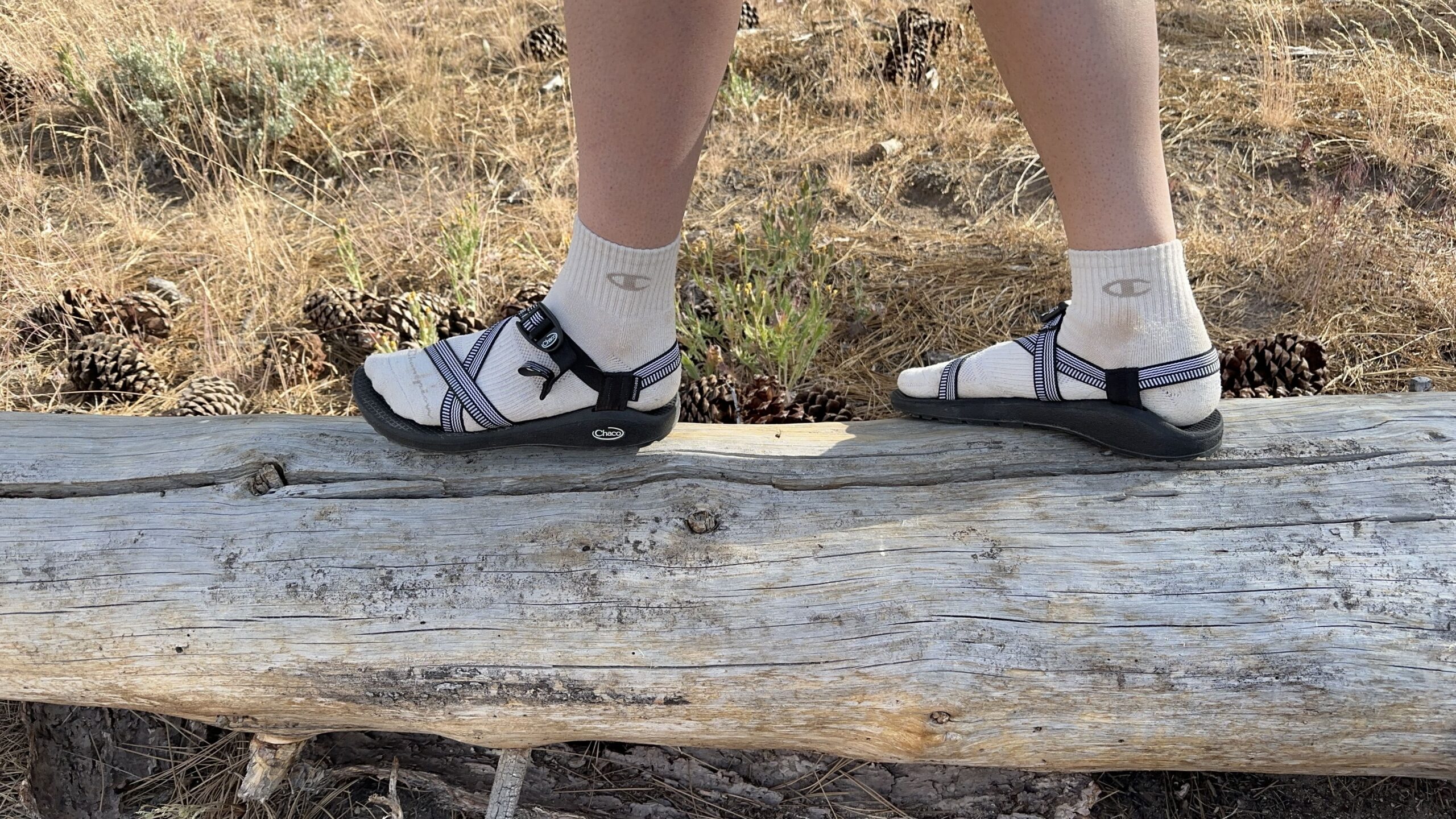 A woman walks along a log wearing black sandals.