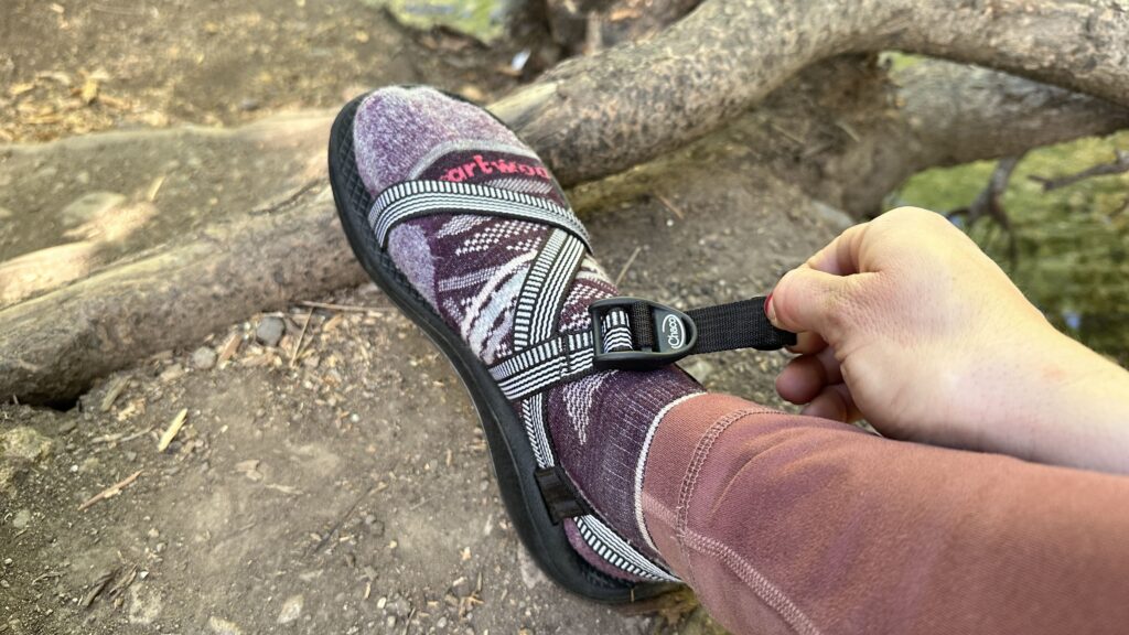 A woman in purple socks pulls the tab on her sandals to tighten the straps to her feet.