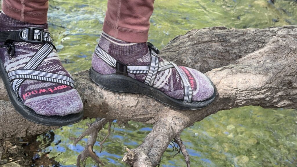 A woman walks along a log wearing black sandals.