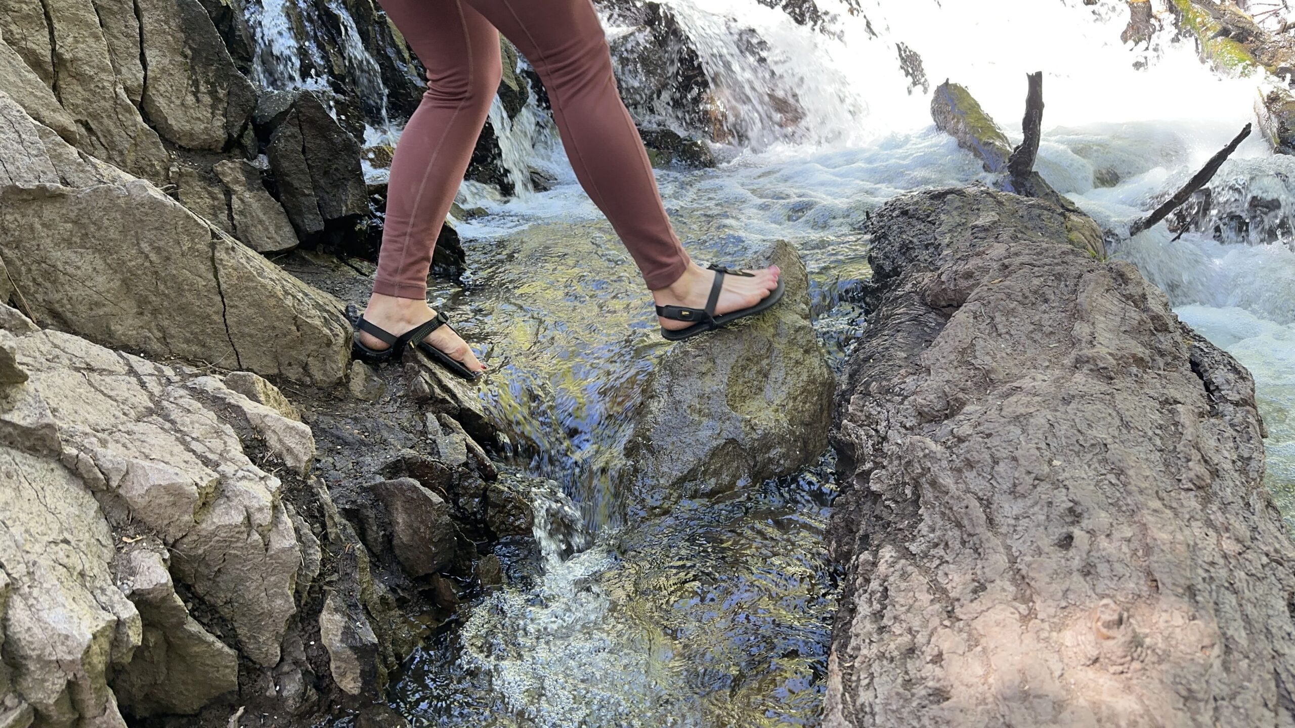 A woman walks across a creek from rock to rock.
