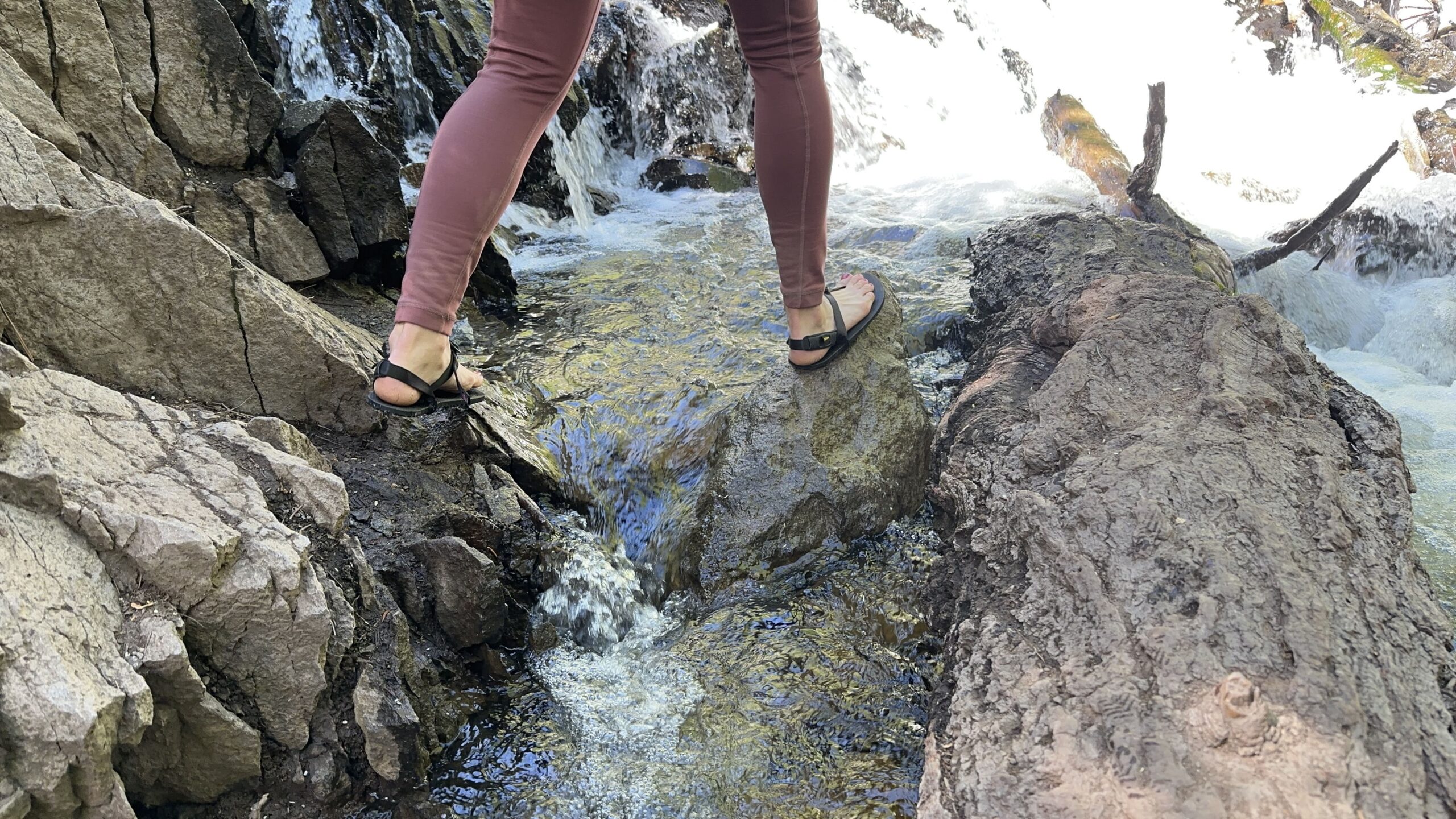 a woman walks across a creek from rock to rock