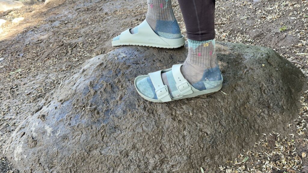 A woman stands on a rock wearing blue sandals and socks