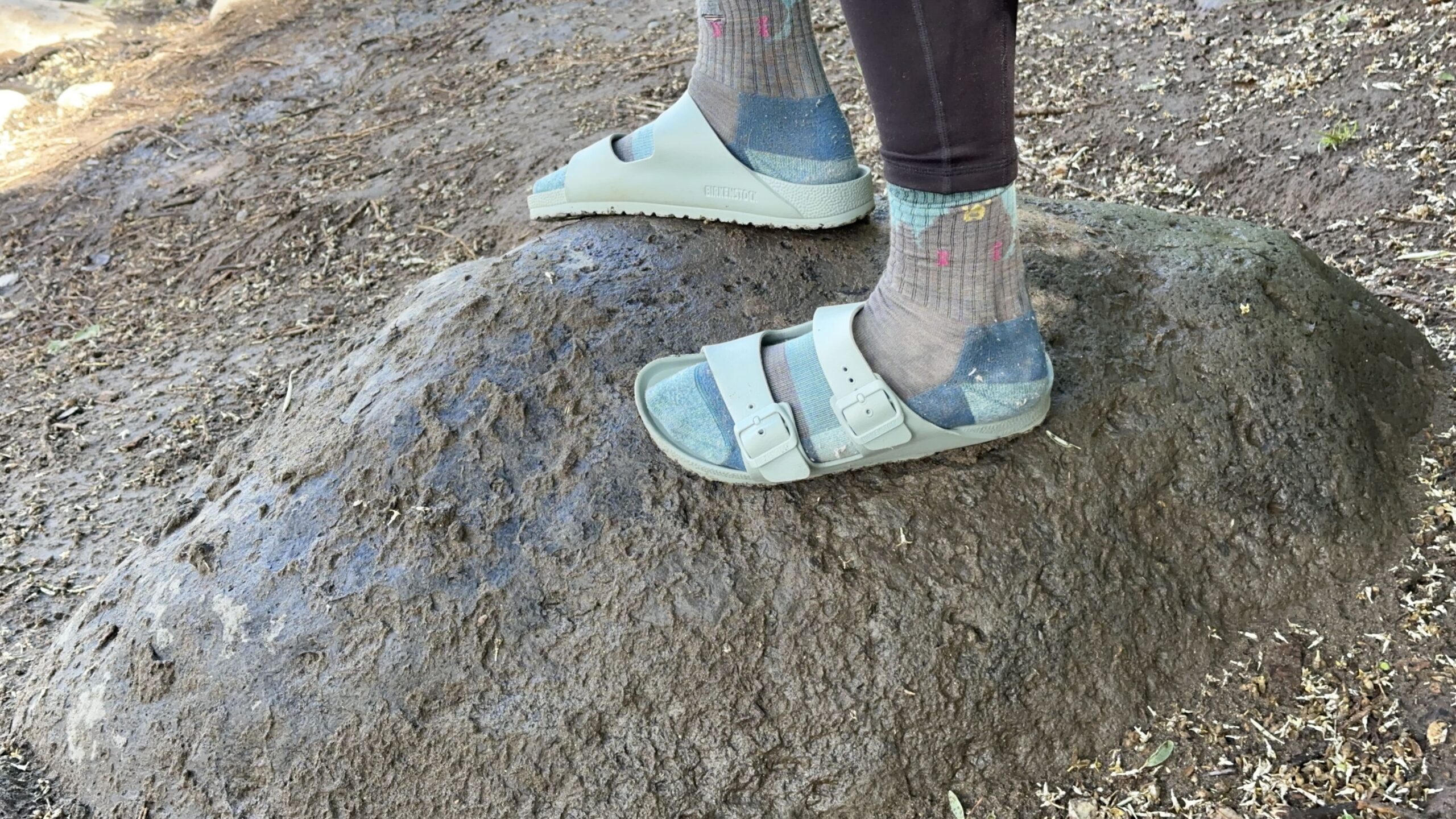 A woman stands on a rock wearing blue sandals and socks