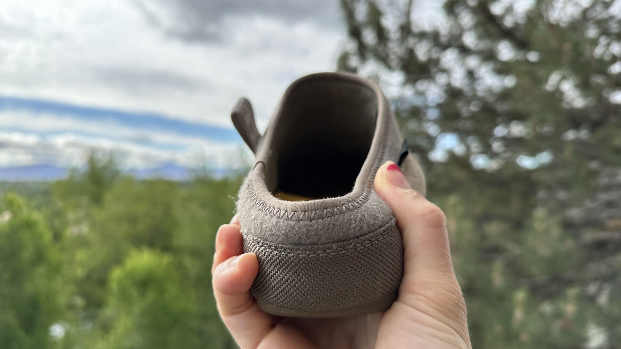 A woman holds the back of a slipper to the camera with trees in the background.