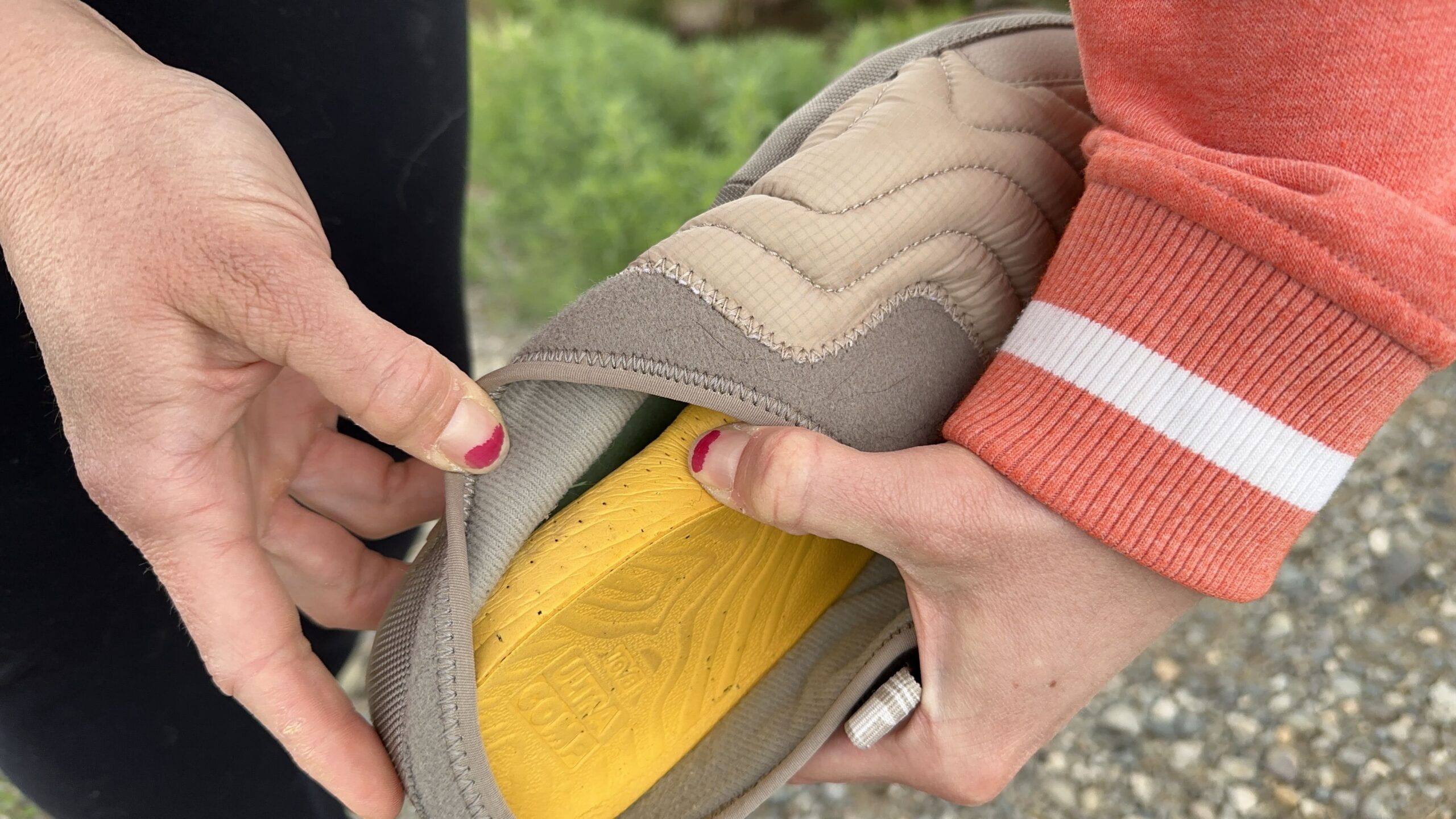 A woman pulls out the yellow footbed of a slipper to show how thick it is.