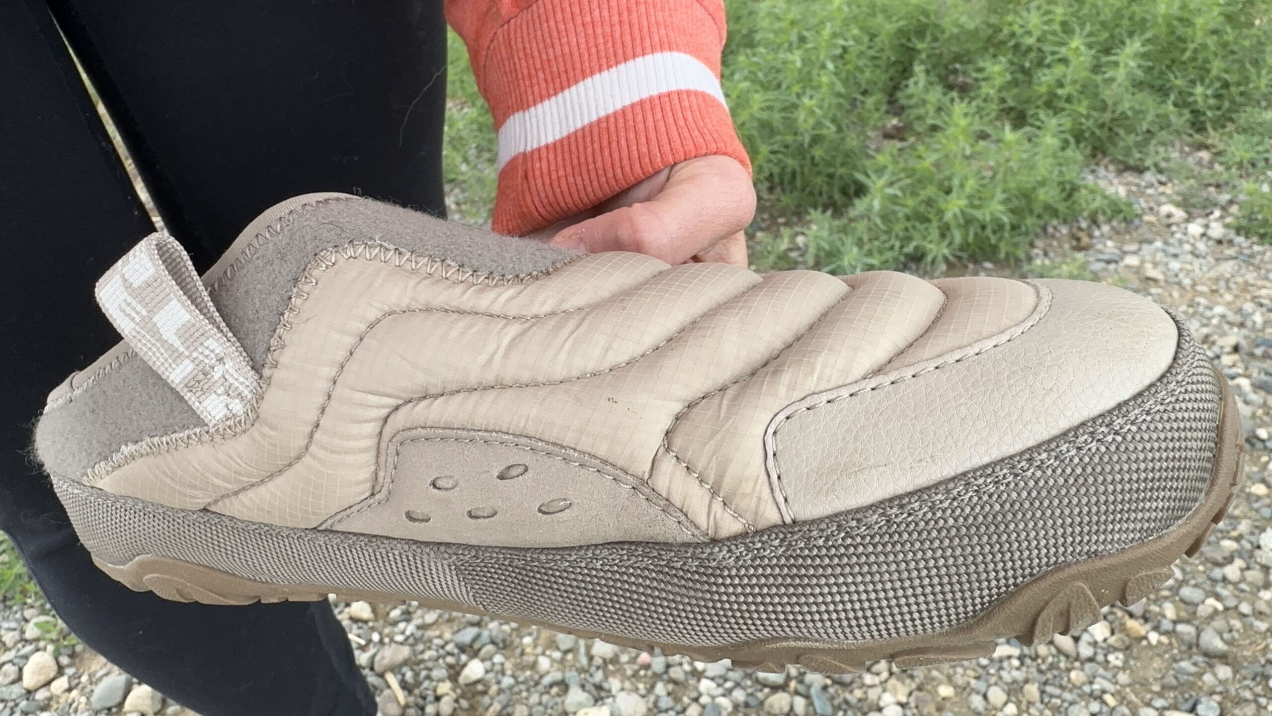 a woman holds up a shoe close to the camera to show its quilted upper