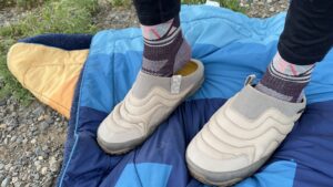 A woman slips on a pair of slippers on top of a blue blanket.