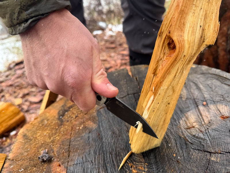 Kershaw Bel Air being used to shave a thin curl from a piece of split wood on a stump in wet conditions.