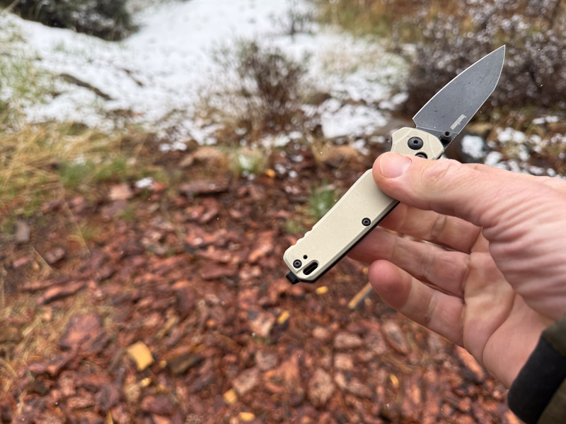 Kershaw Bel Air held open in one hand outdoors with snowy ground in the background.