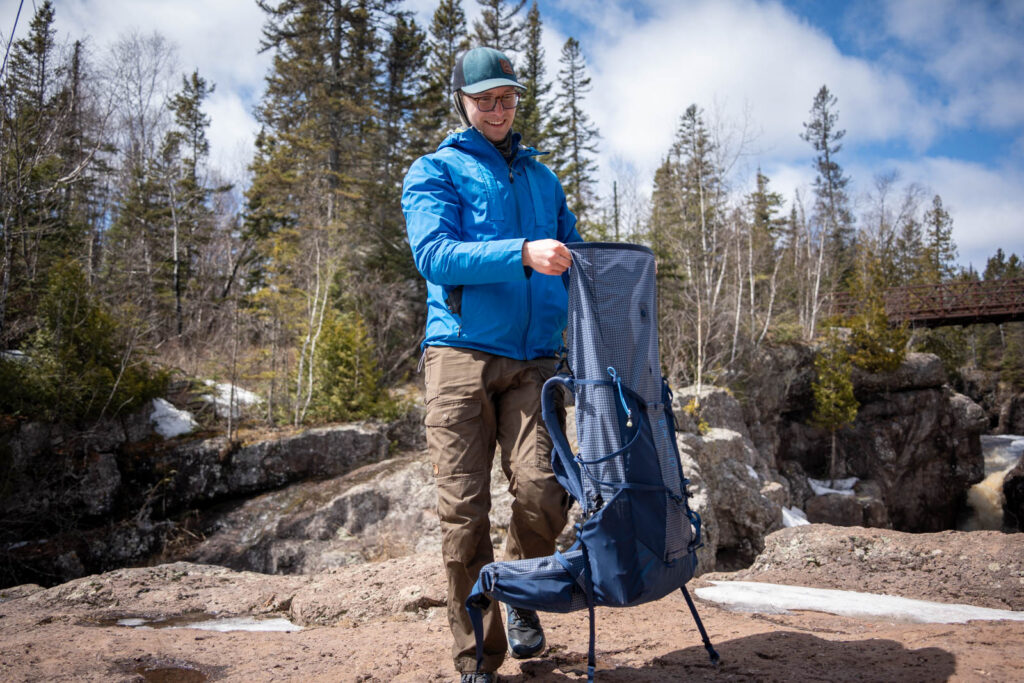 A man holds a backpack in front of a river gorge