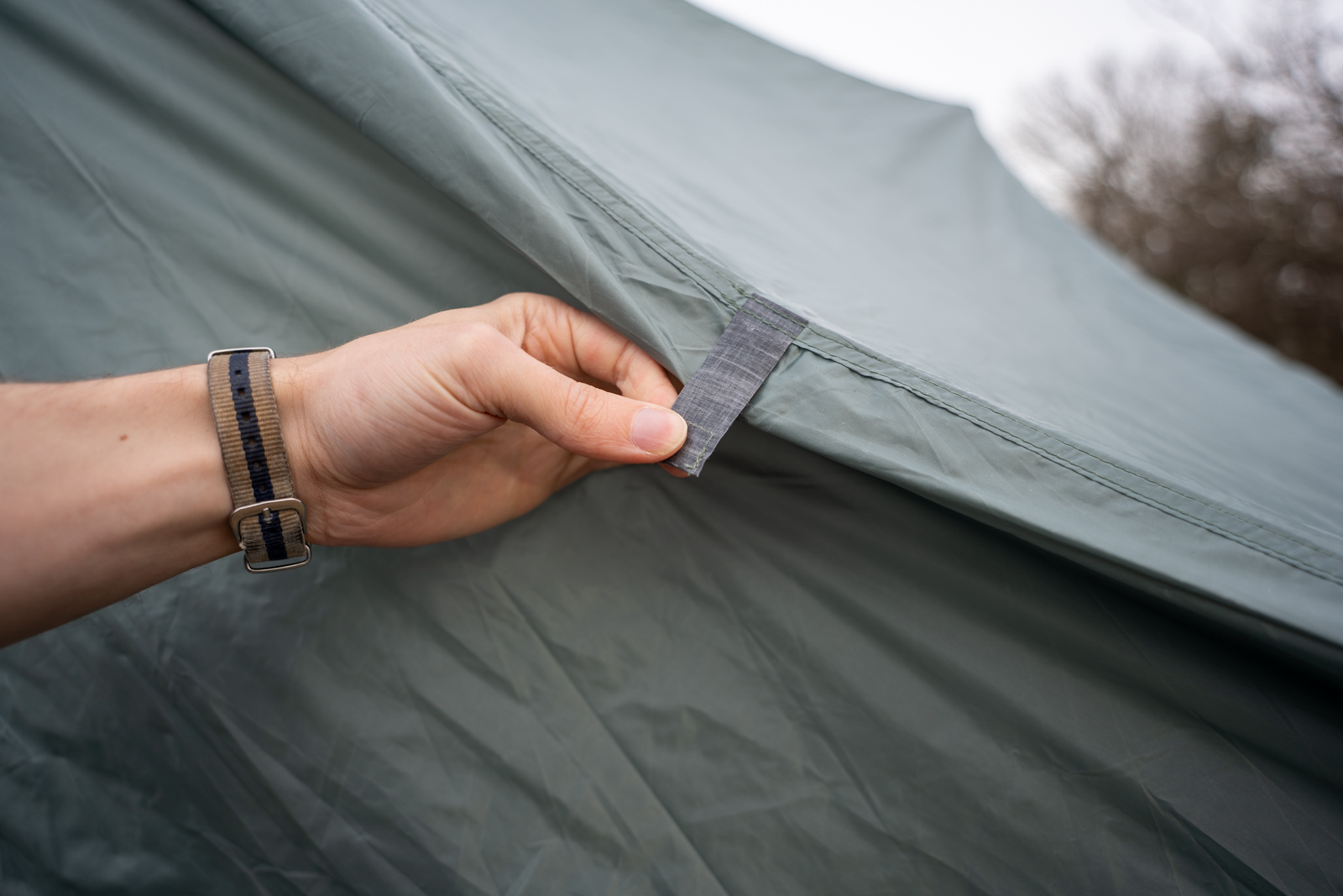 A hand holds a magnetic door toggle on a tent