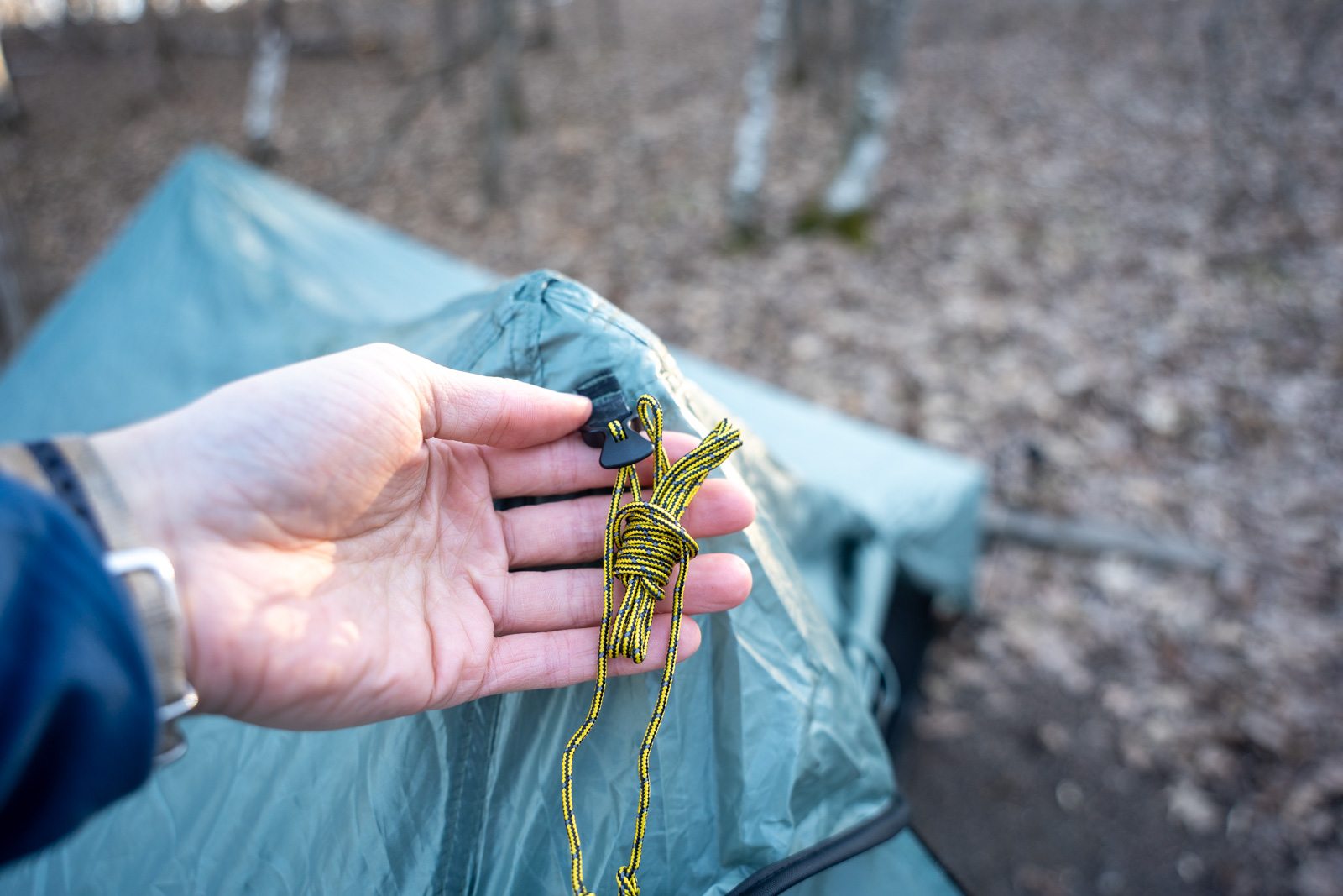 A hand holds some yellow cord connected to the peak of a tent