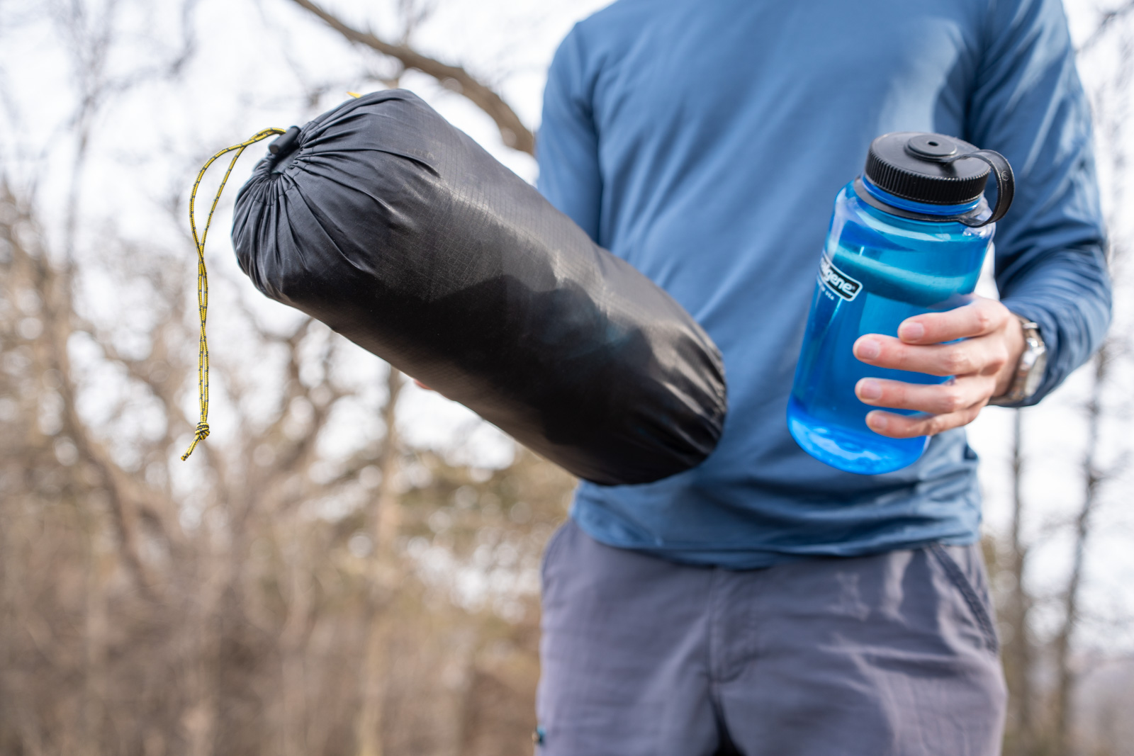 A man holds a tent and a water bottle