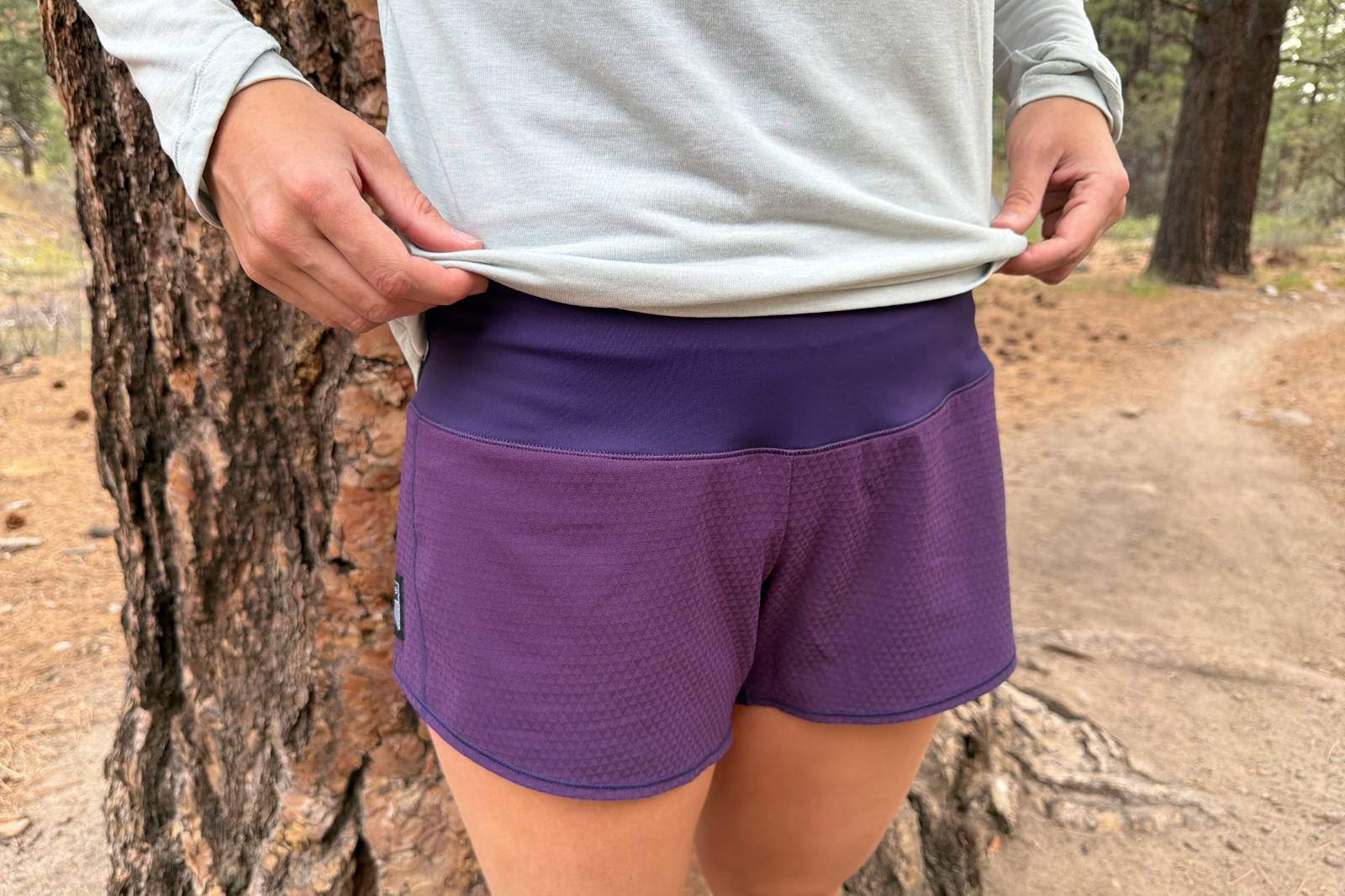 Close-up image of a woman holding up the bottom hem of her shirt to reveal the wide waistband of her running shorts.