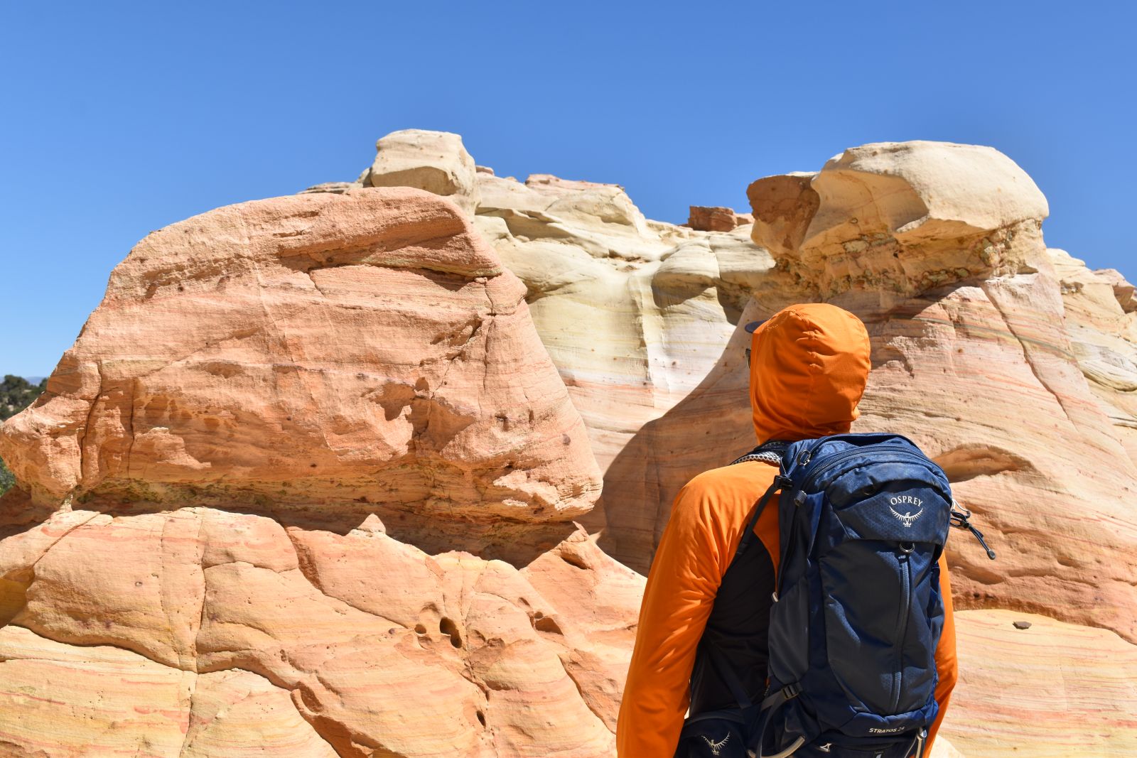 A hiker in a hoodie stares at a volcanic rock formation wearing an Osprey Stratos 24 daypack