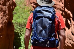 Close up of a man in a red hiking shirt wearing a blue Osprey Stratos daypack in a redrock slot canyon