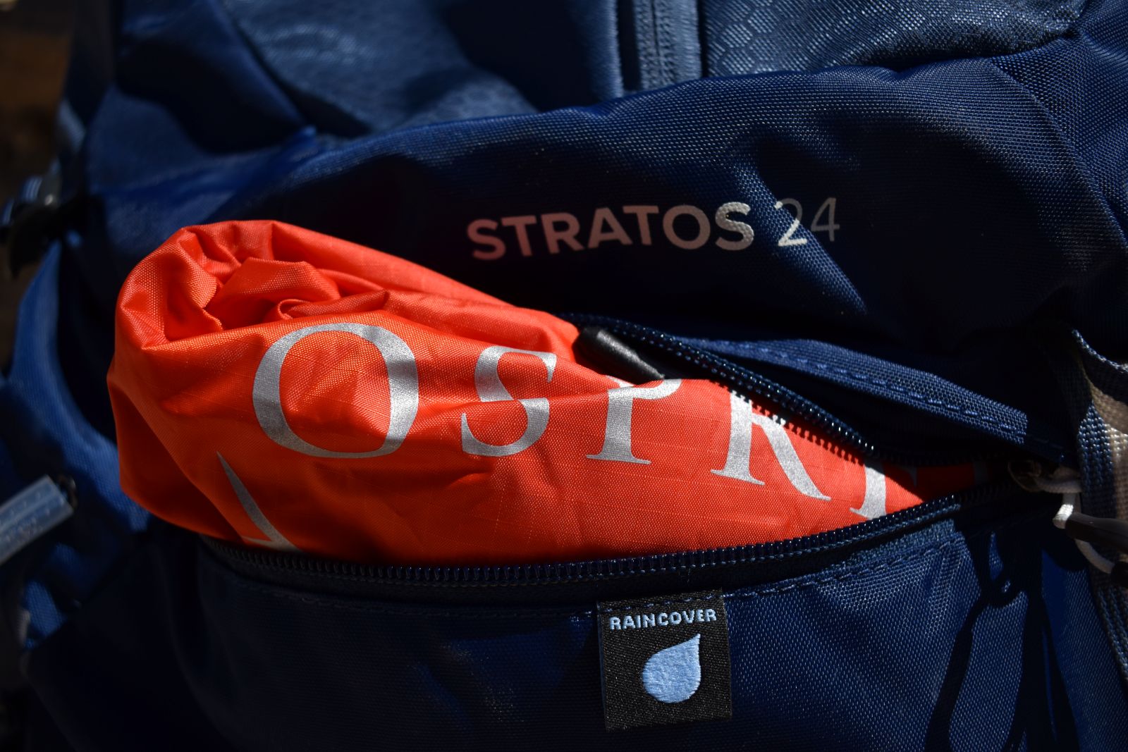 The orange rain cover of the Osprey Stratos visible in its zippered raincover pocket