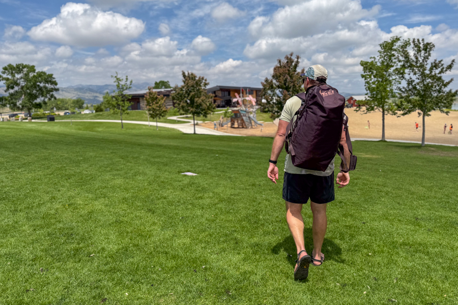 Person wearing the REI Co-op Big Haul 60 as a backpack while walking through a park near a lake.