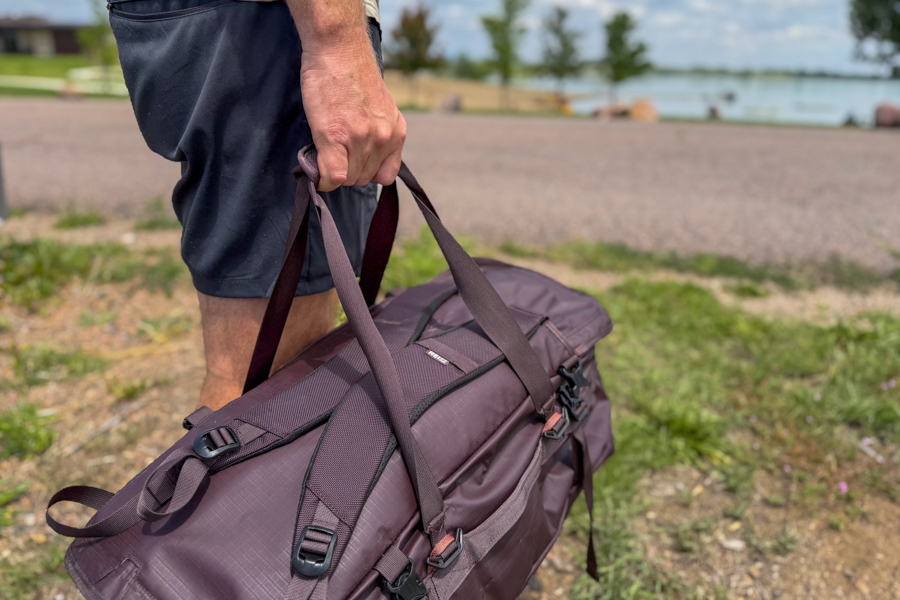 Close-up of a person carrying the REI Co-op Big Haul 60 by its tote handles near a lake.