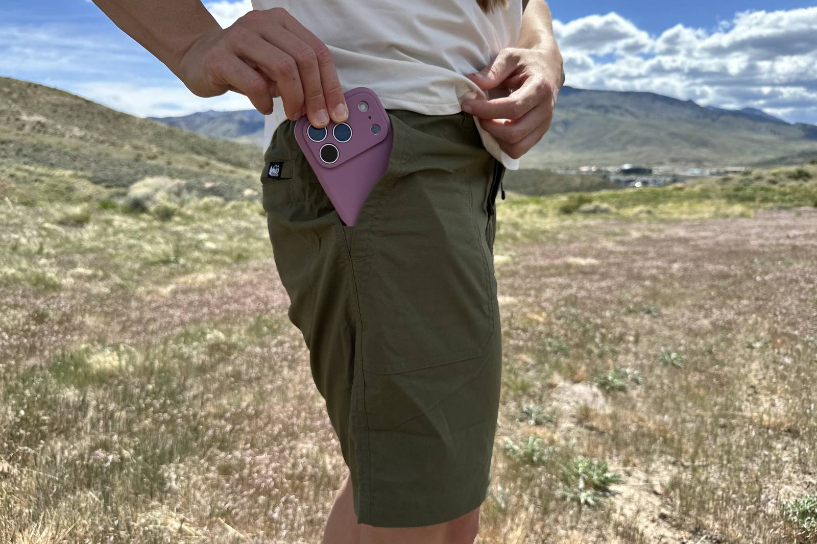 Imagen de primer plano de una mujer que pone un teléfono inteligente en el bolsillo de sus pantalones cortos de senderismo.