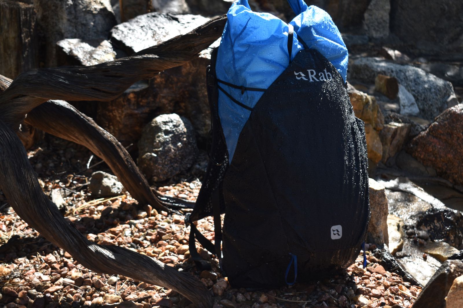 The waterproof Rab Syclon XP daypack is dripping with water in a rock garden.