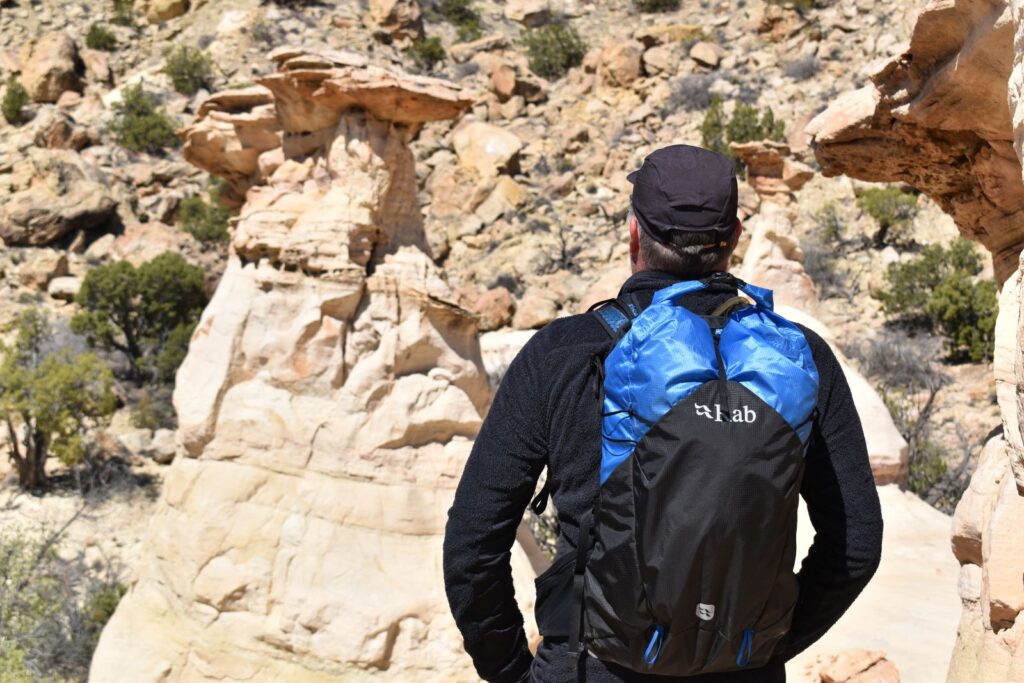 A hiker stares at a hoodoo while wearing a blue and black Rab Sylon XP daypack.