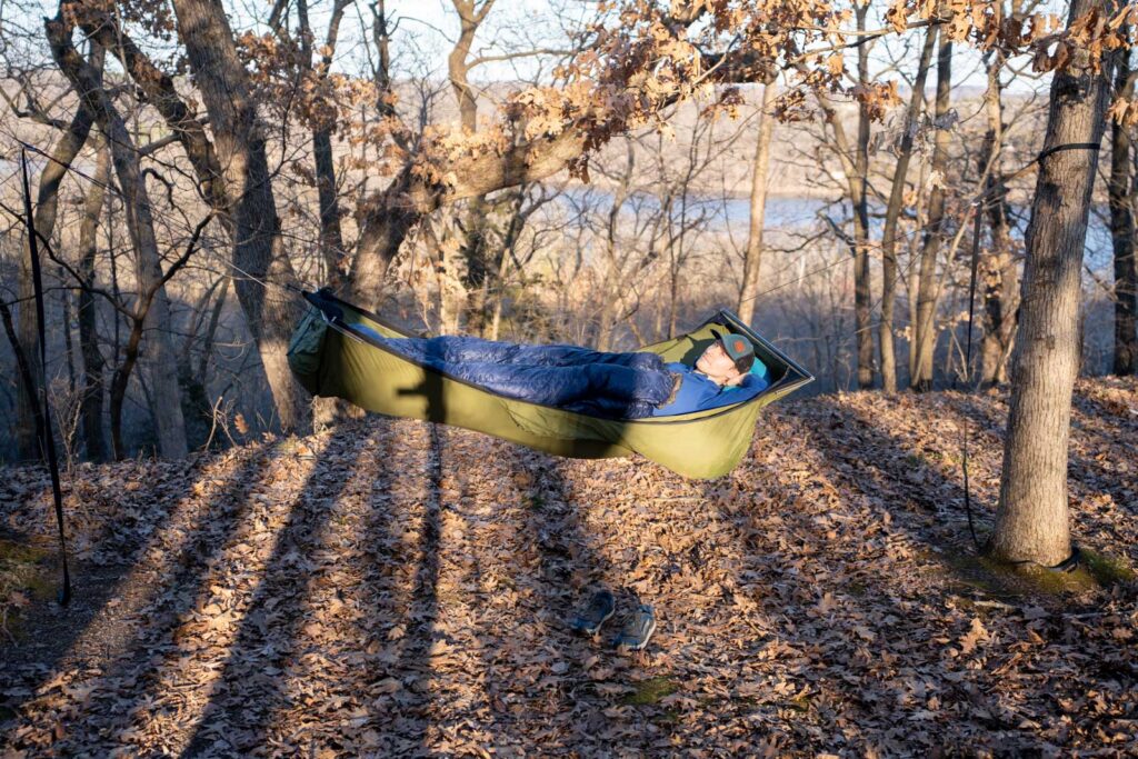 A man lies in a hammock in the woods at sunset.