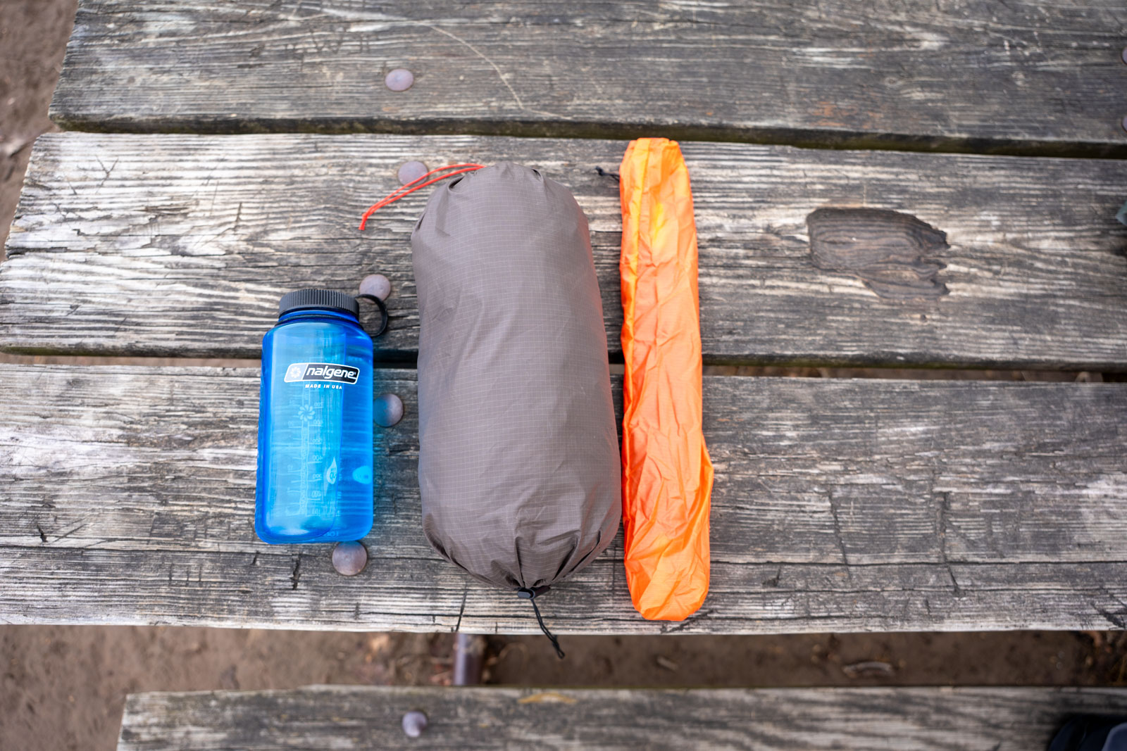 A water bottle a hammock and hammock poles sit on a picnic table.