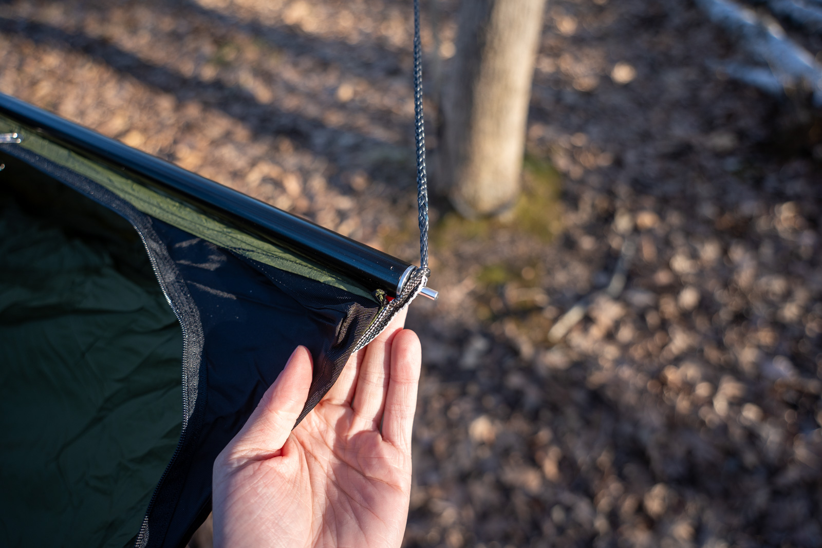 A hand holds the edge of a hammock and spreader bar.