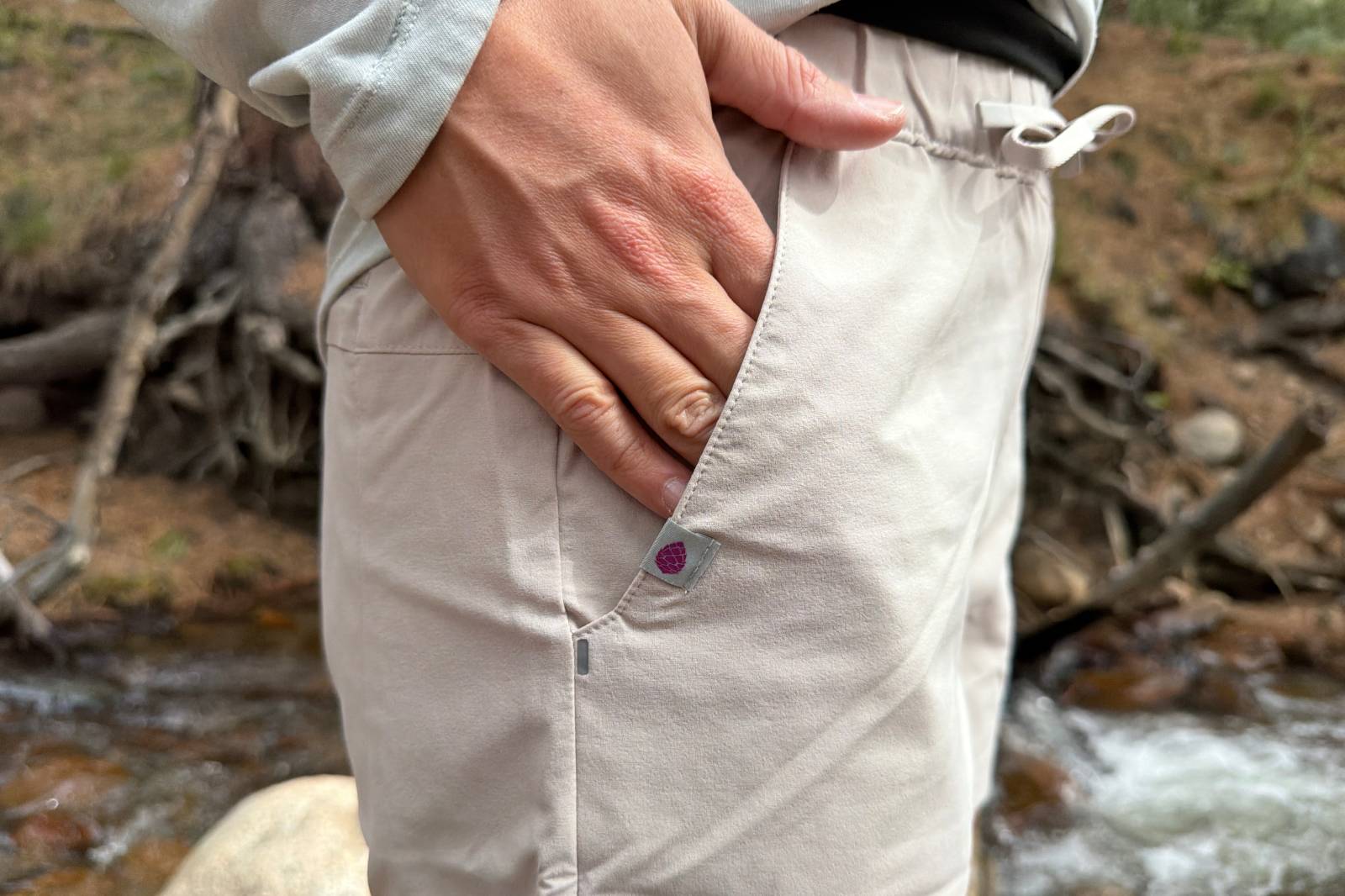 Close-up image of a hand reaching into the hand pocket on a pair of beige hiking shorts.