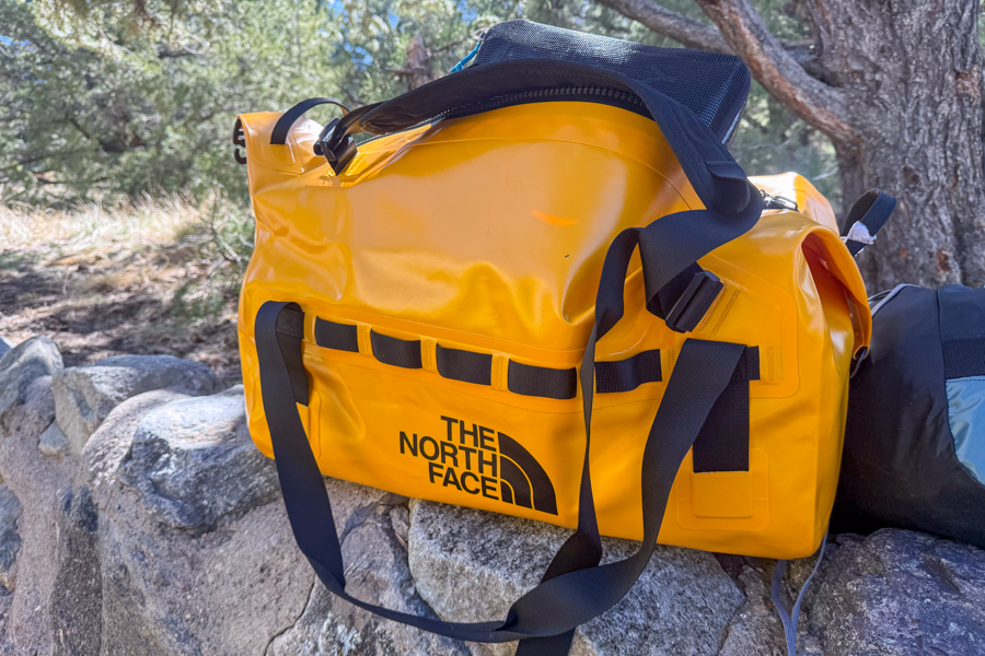 Yellow The North Face Base Camp Waterproof Duffel 50L sitting on rocks under trees.